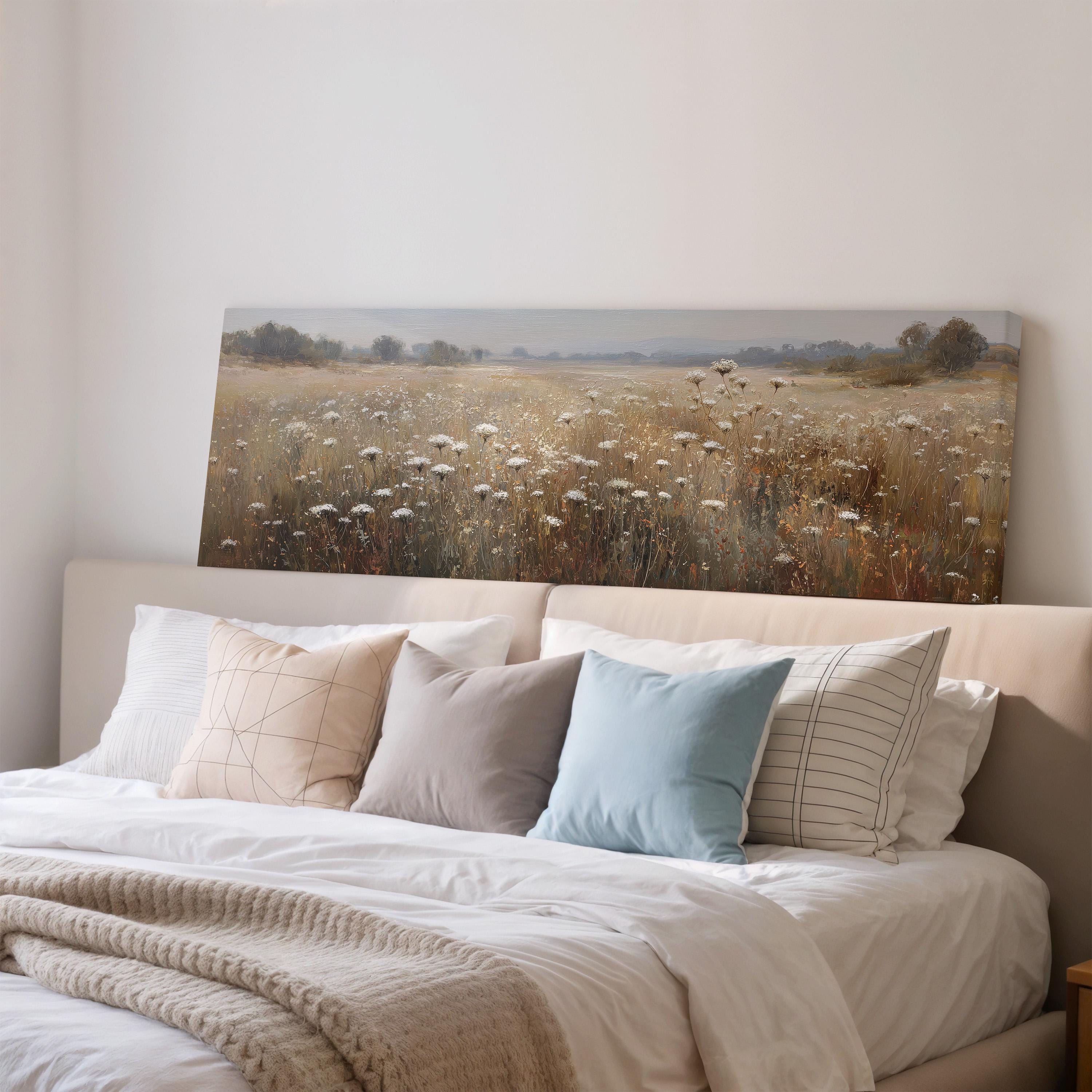 a large bed with a white comforter and pillows, and a painting of a field of flowers above it.