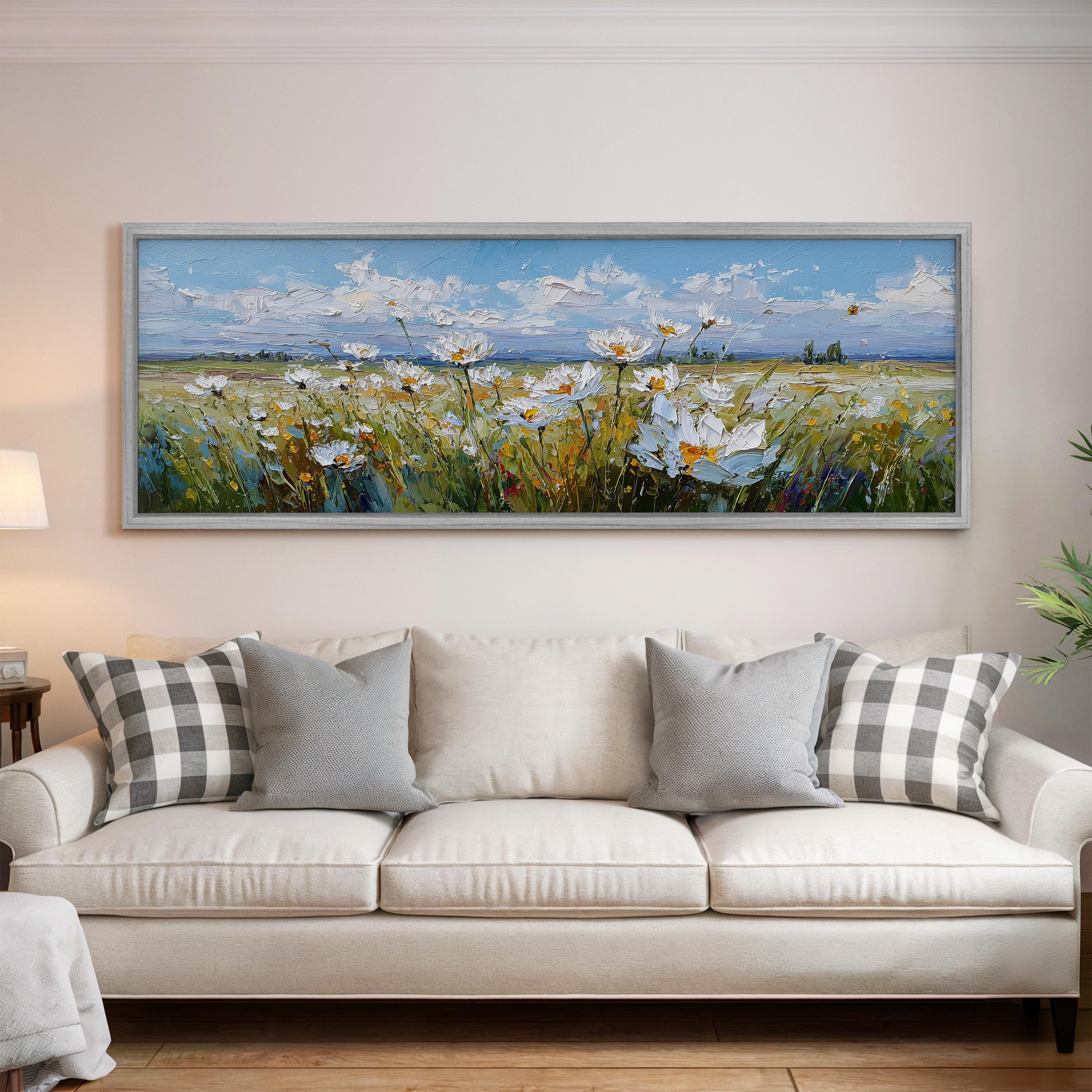 a large painting of a field of flowers hanging on a wall above a white sofa with gray and white plaid throw pillows.