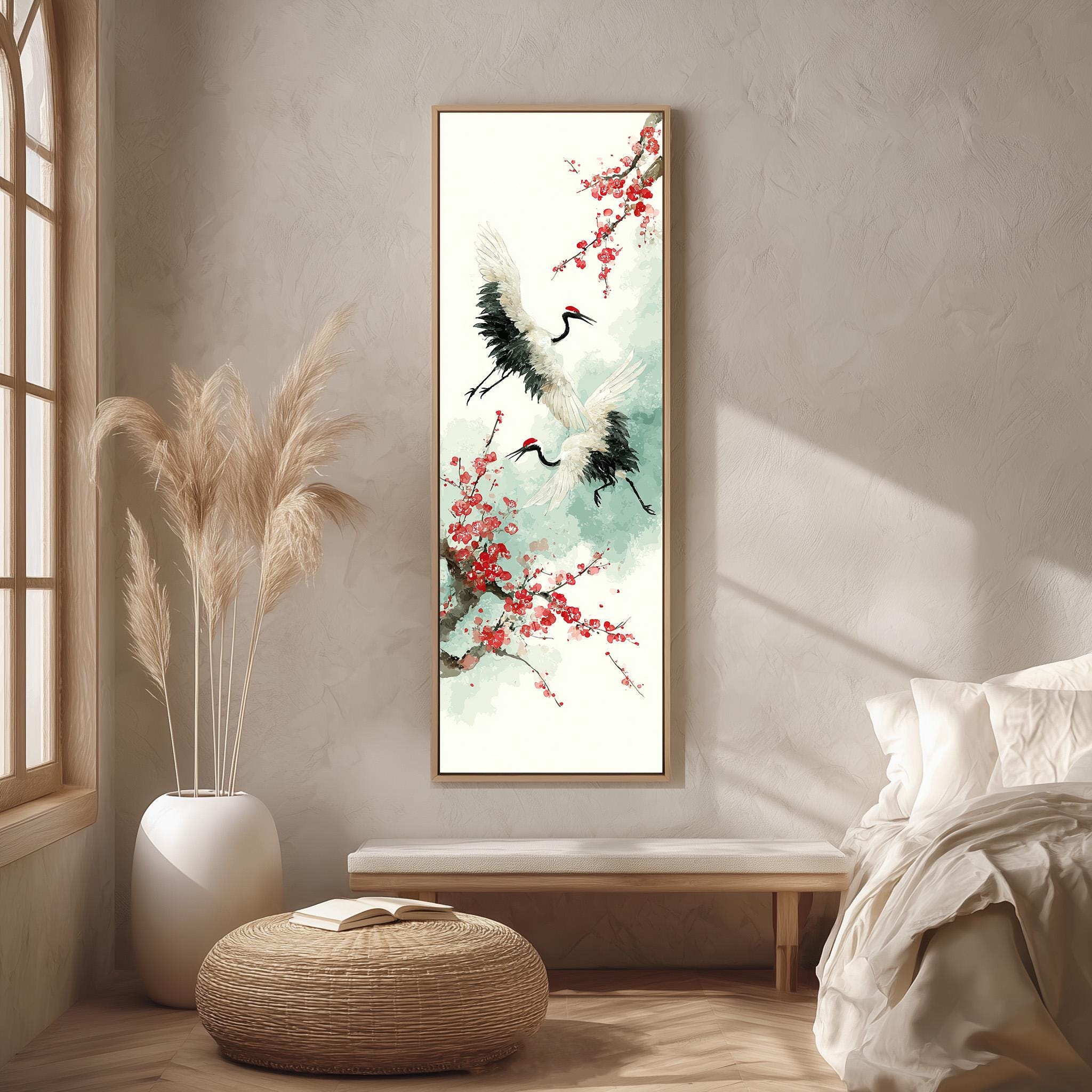 a serene and minimalist bedroom setting with a large painting of two cranes in flight hanging on the wall. The painting is surrounded by a white vase filled with tall, light-colored reeds, and a woven ottoman is placed in front of the painting. The room also includes a bed with white linens and a window that allows natural light to enter the space.