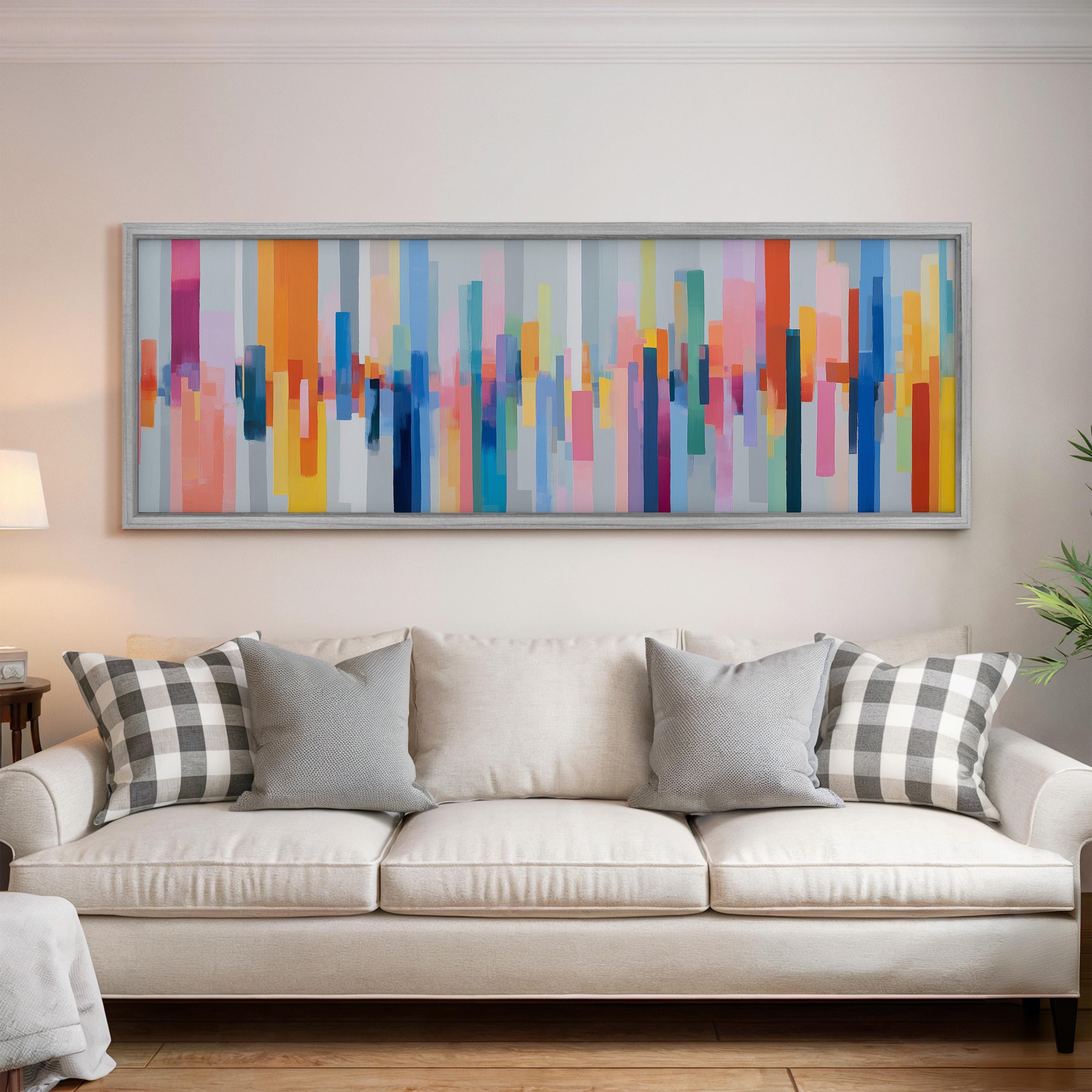 a large, colorful abstract painting hanging on a wall above a white couch with gray and black plaid throw pillows.