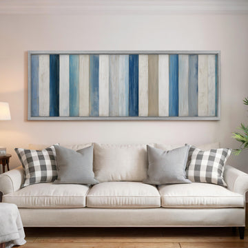 a living room with a white sofa adorned with gray and black plaid throw pillows. Above the sofa, there is a large framed artwork with vertical stripes in various shades of blue and white.