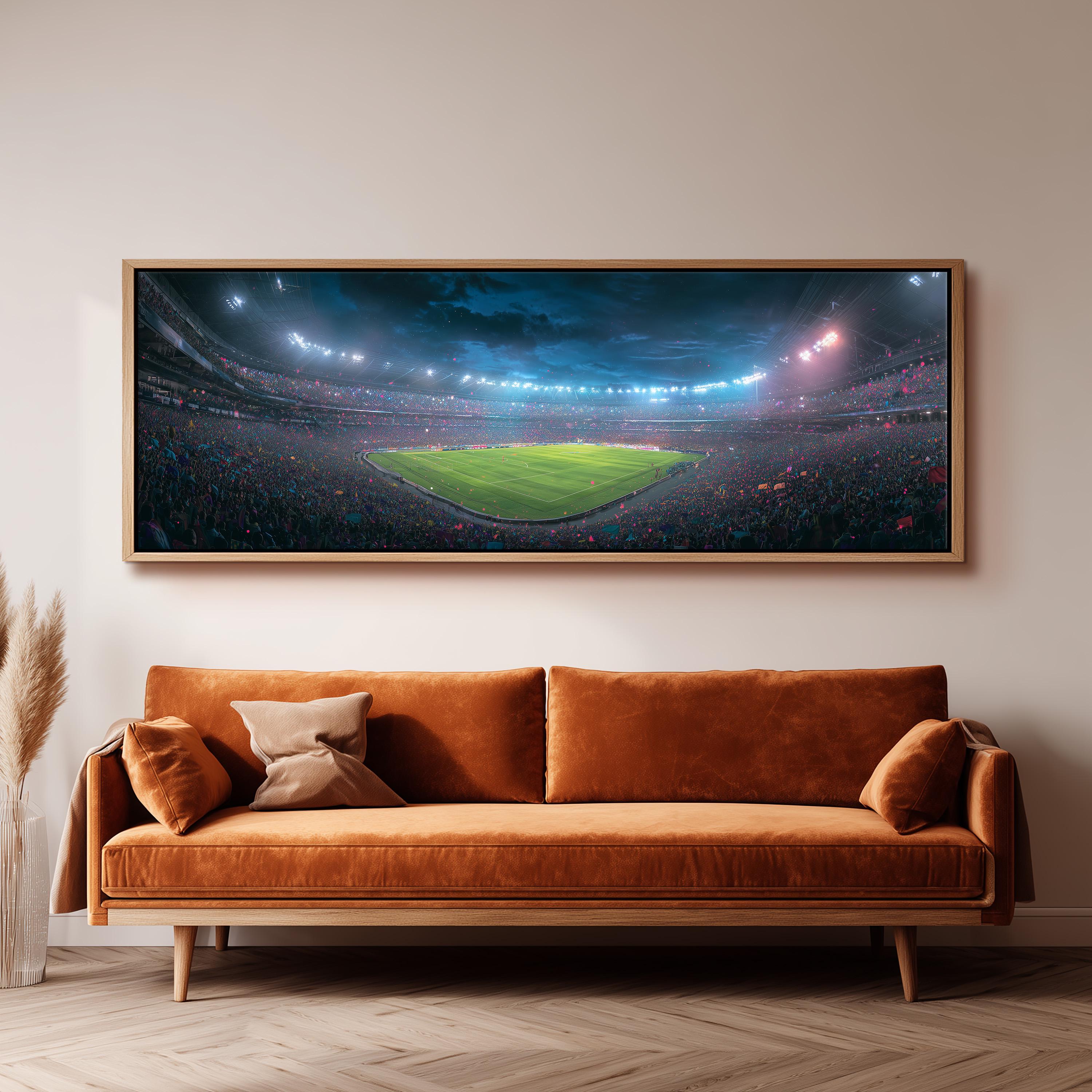 a large, framed picture of a soccer stadium with a crowd of spectators, hanging on a wall above a brown sofa.