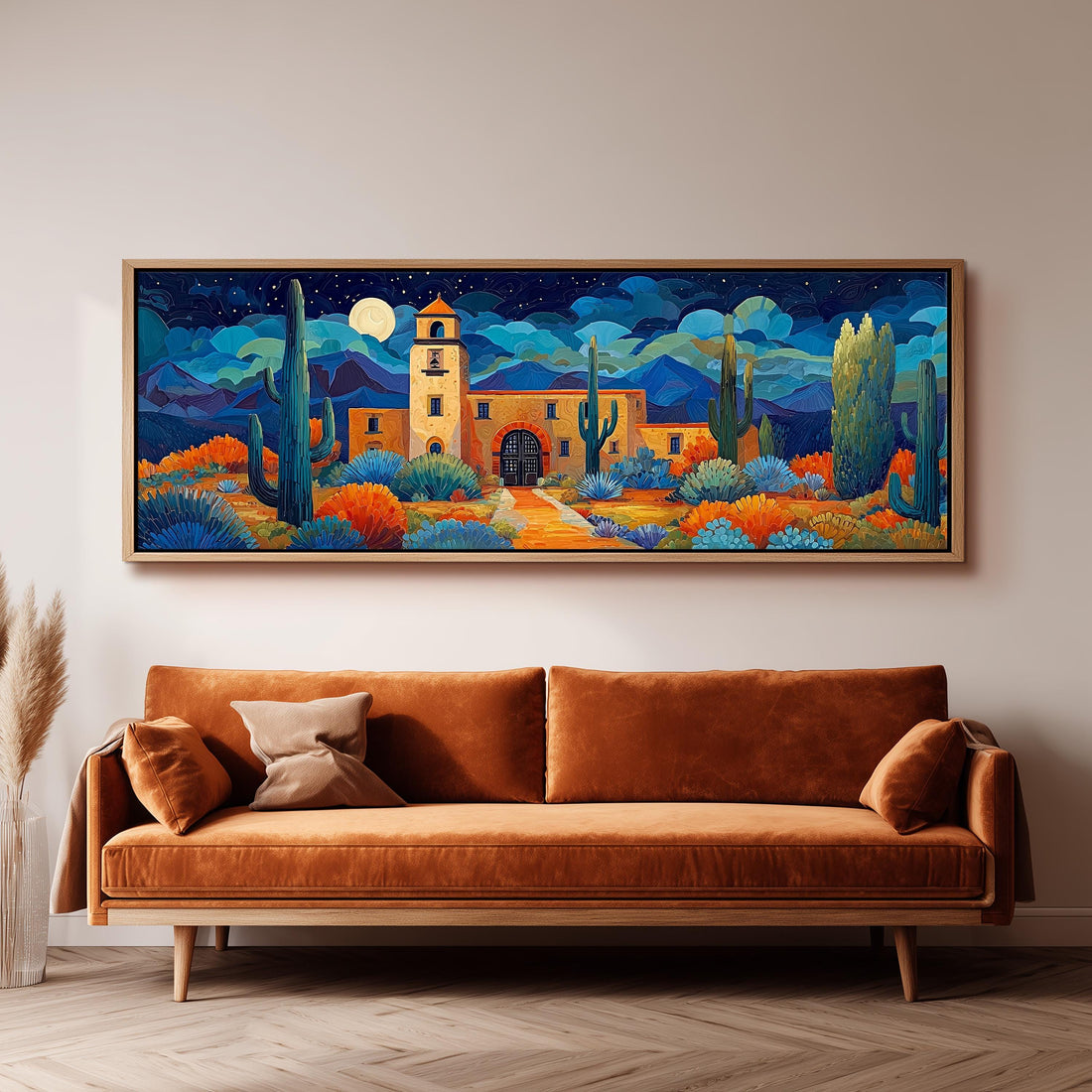 a large, colorful painting of a desert landscape with a building, cacti, and a moon in the night sky. The painting is hung on a wall above a brown sofa with a wooden frame.