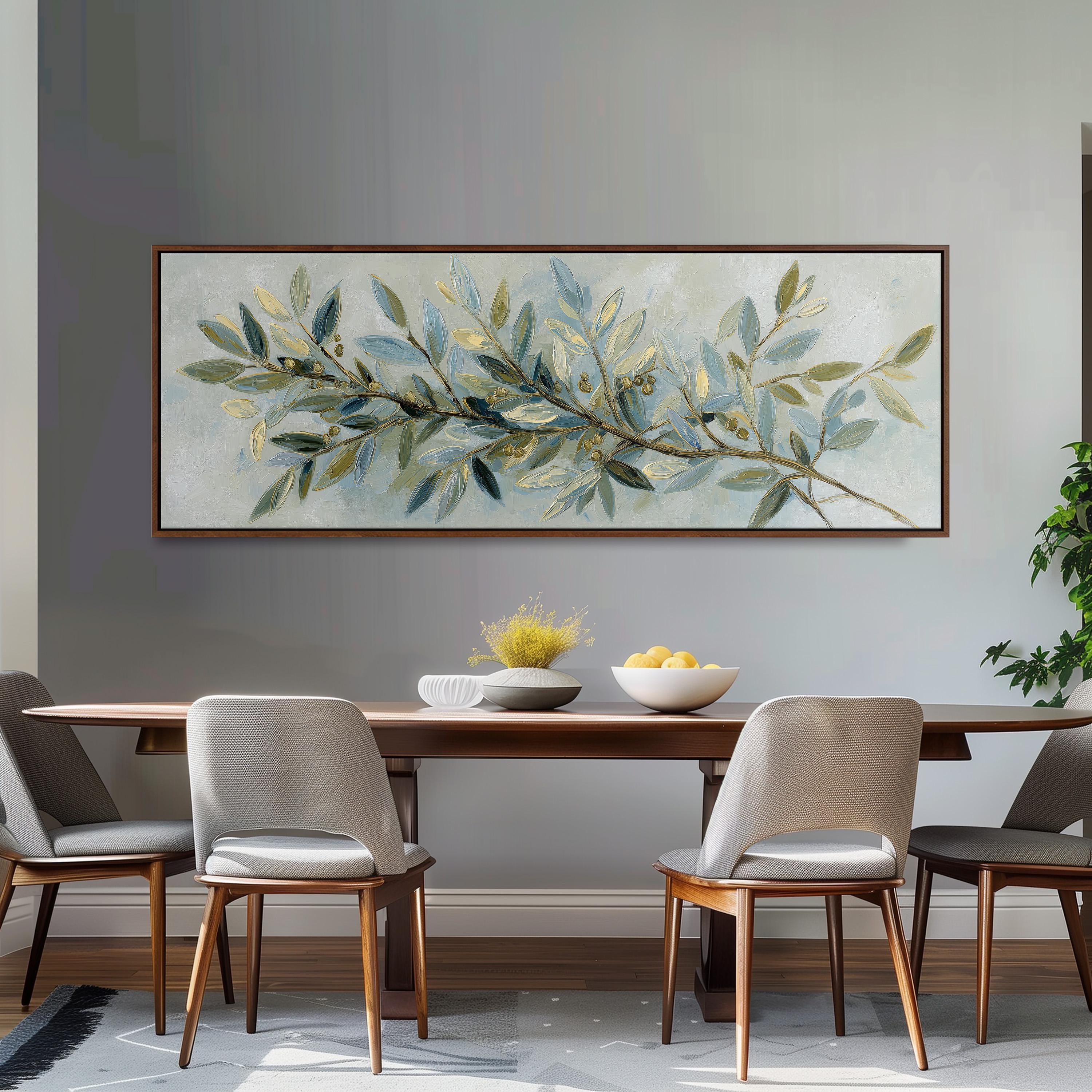 a dining room with a large painting of a branch of green leaves hanging on the wall above a wooden dining table with four chairs. The table is set with a bowl of fruit and a vase of flowers, creating a cozy and inviting atmosphere.