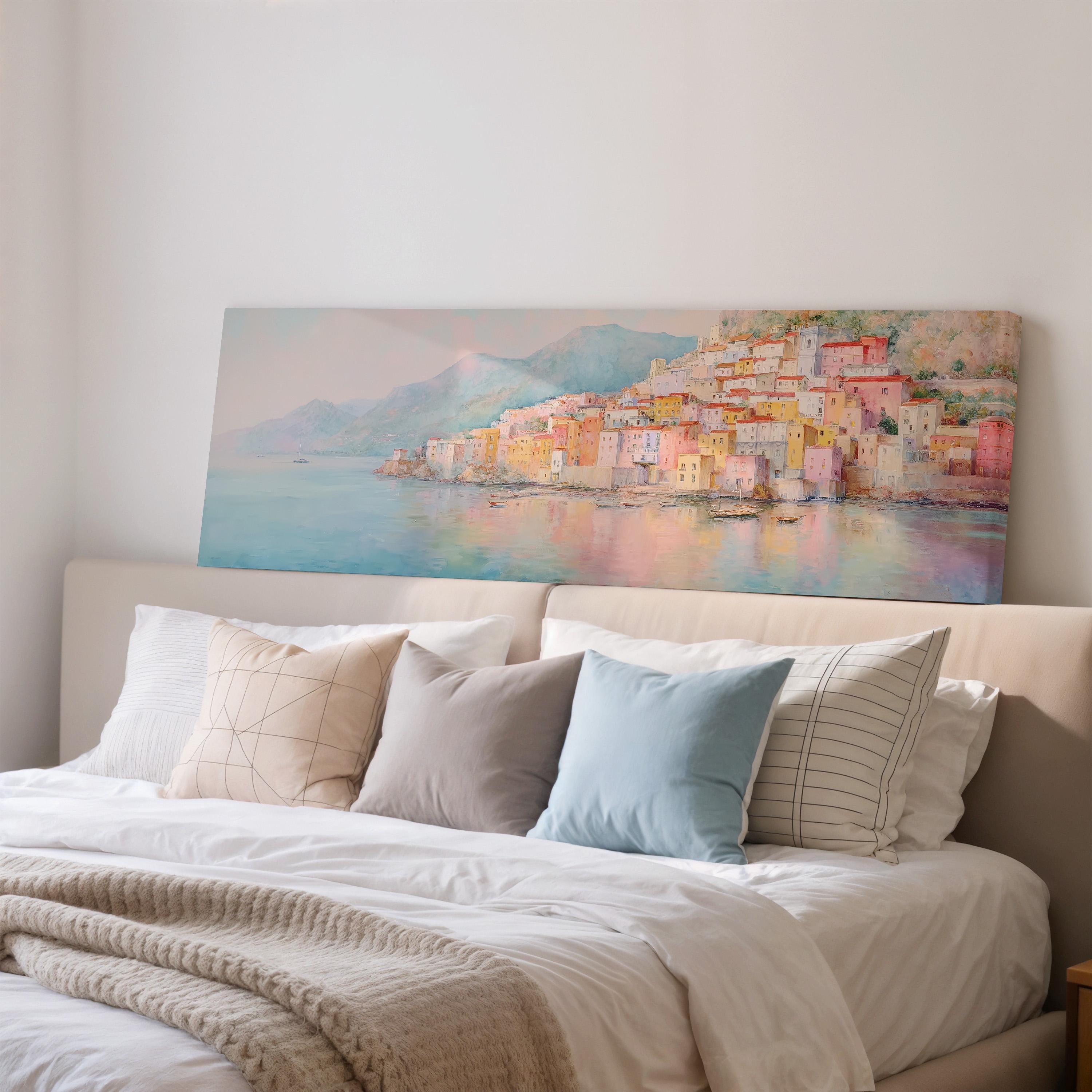 a large painting of a coastal town on the wall above a bed with white pillows and a gray blanket.