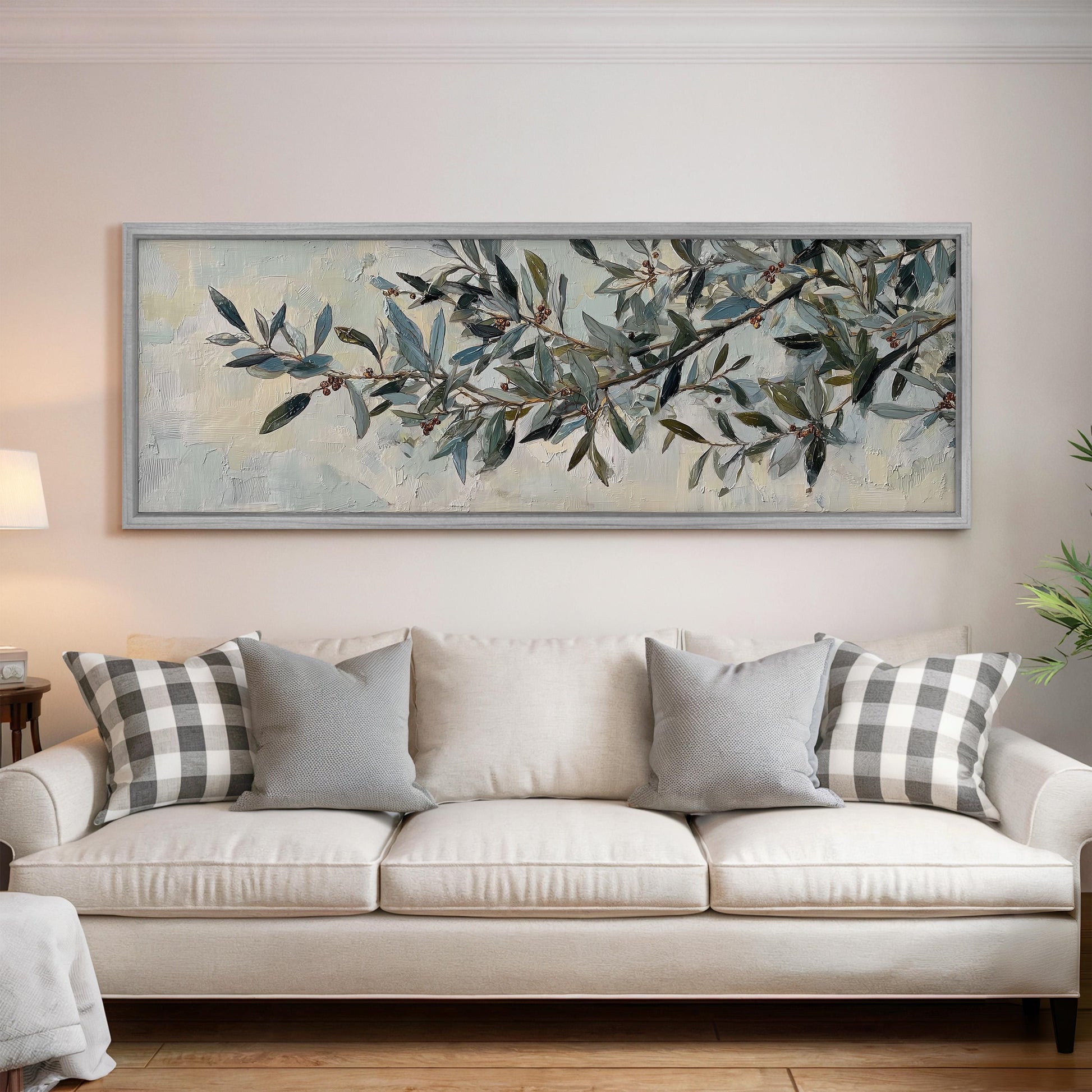 a large painting of a tree branch with green leaves and brown branches hanging above a white sofa with gray and white plaid throw pillows.