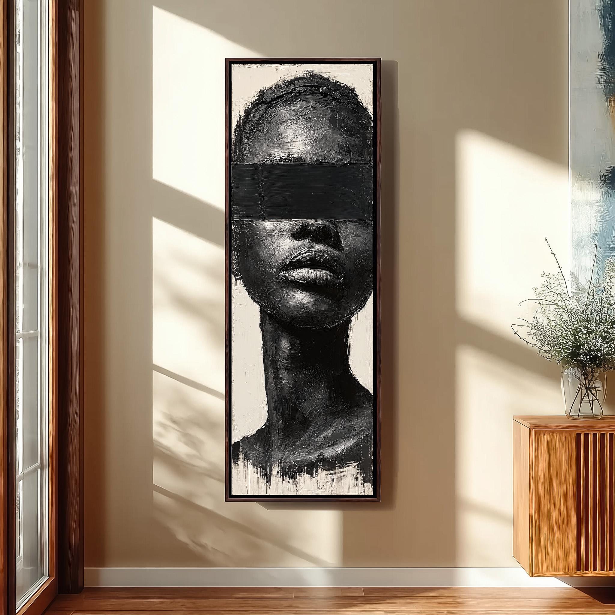 a large black and white portrait of a woman's face, hanging on a wall in a room with a wooden cabinet below it.