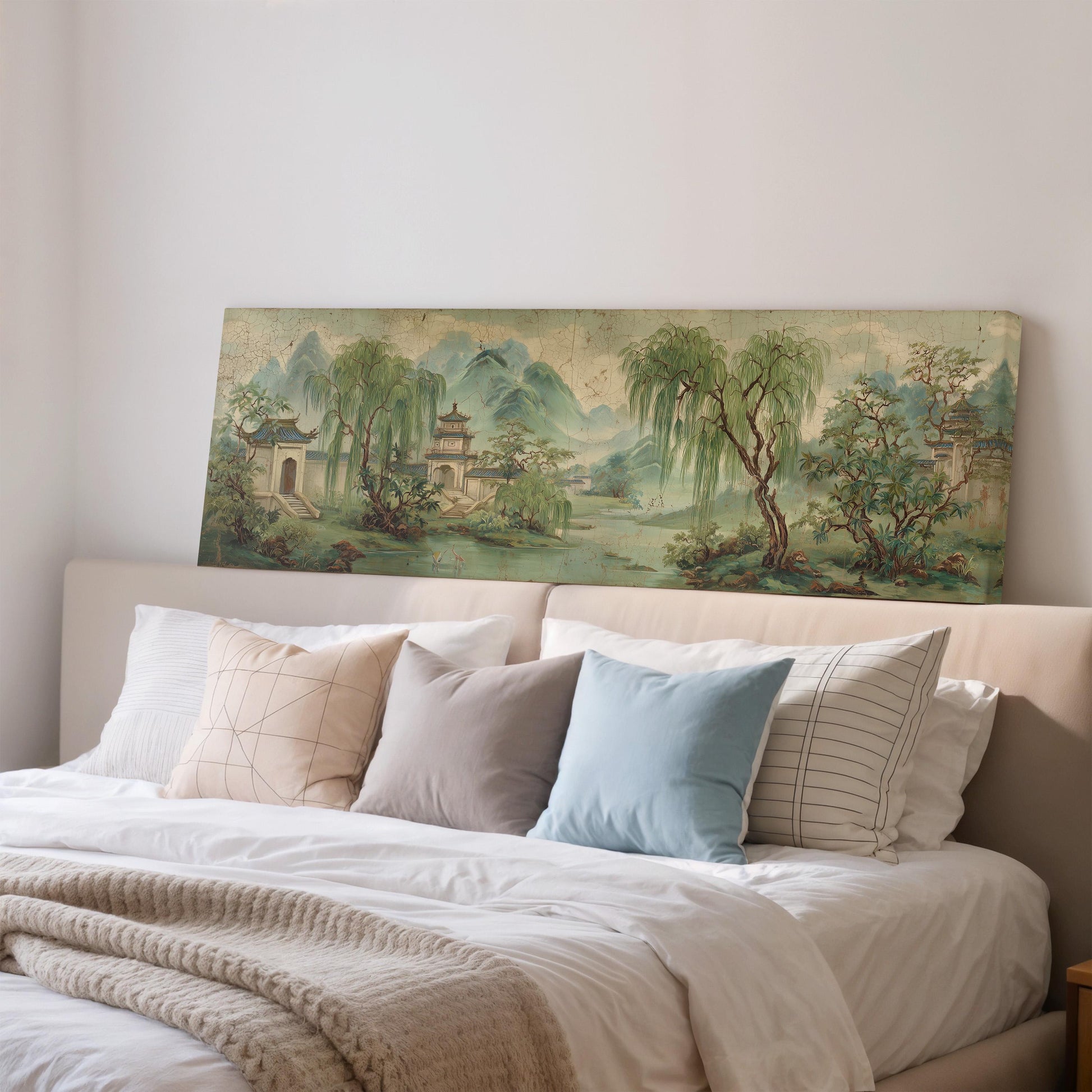 a large painting of a serene landscape hanging on a wall above a bed with white pillows and a gray blanket.