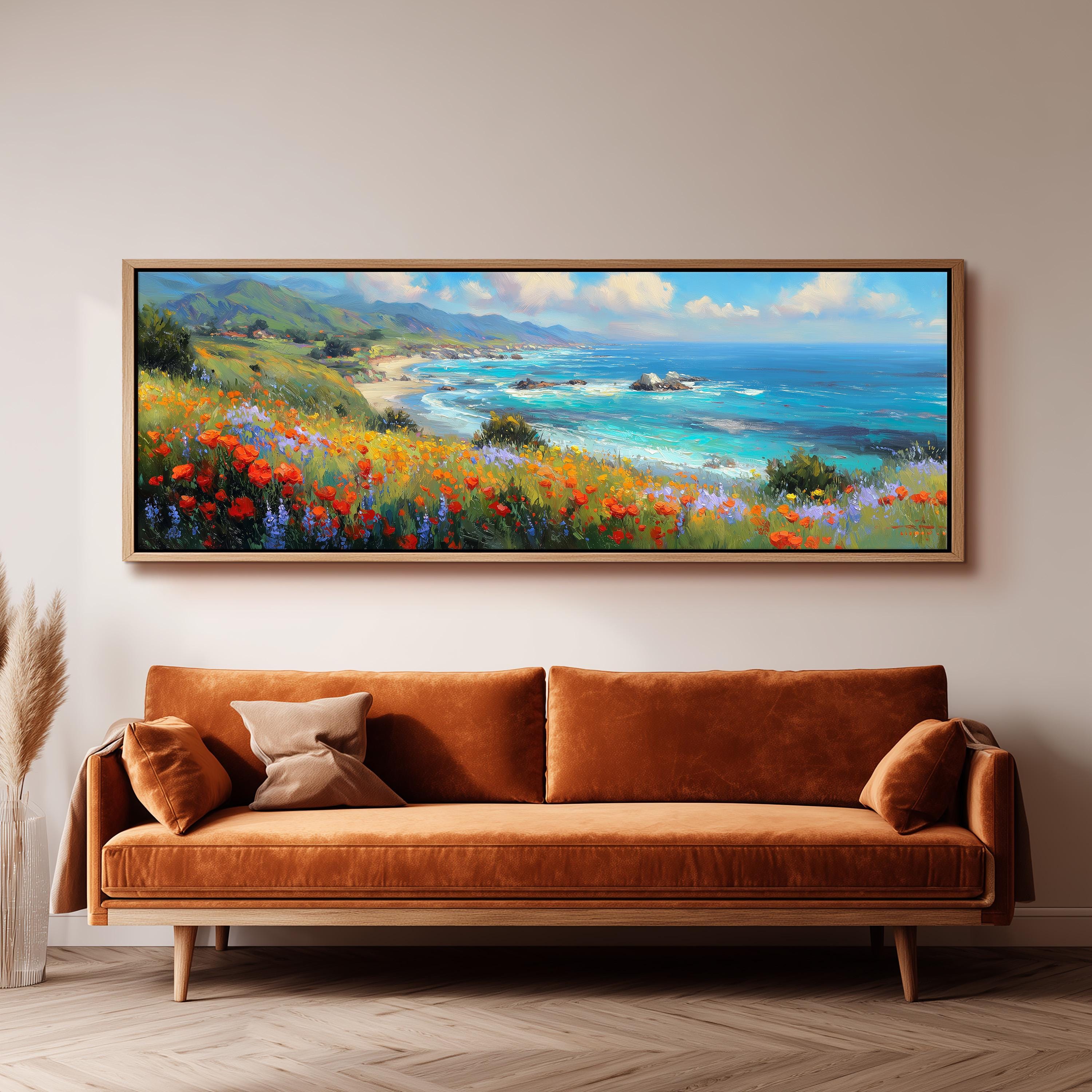 a large, framed painting of a coastal landscape with a beach, mountains, and a body of water. The painting is hanging on a wall above a brown sofa with a pillow on it.