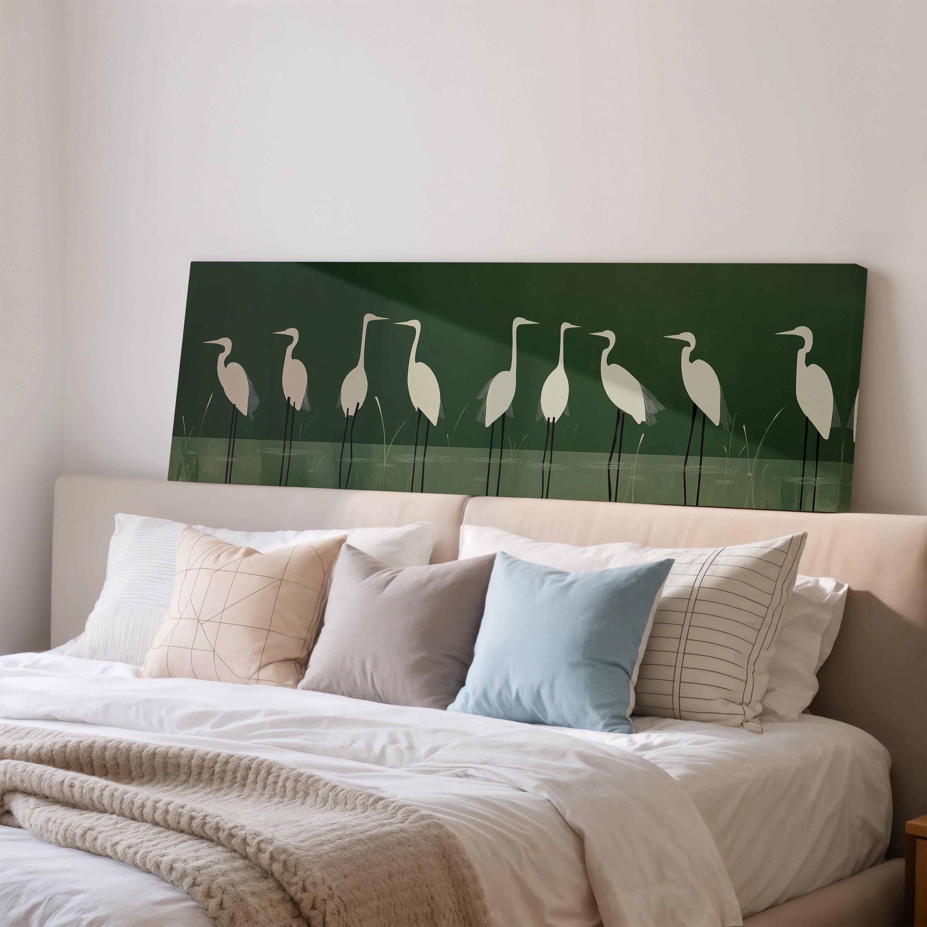 a bedroom with a bed adorned with white pillows and a gray throw blanket. Above the bed, there is a large green canvas with a line of white birds on it.