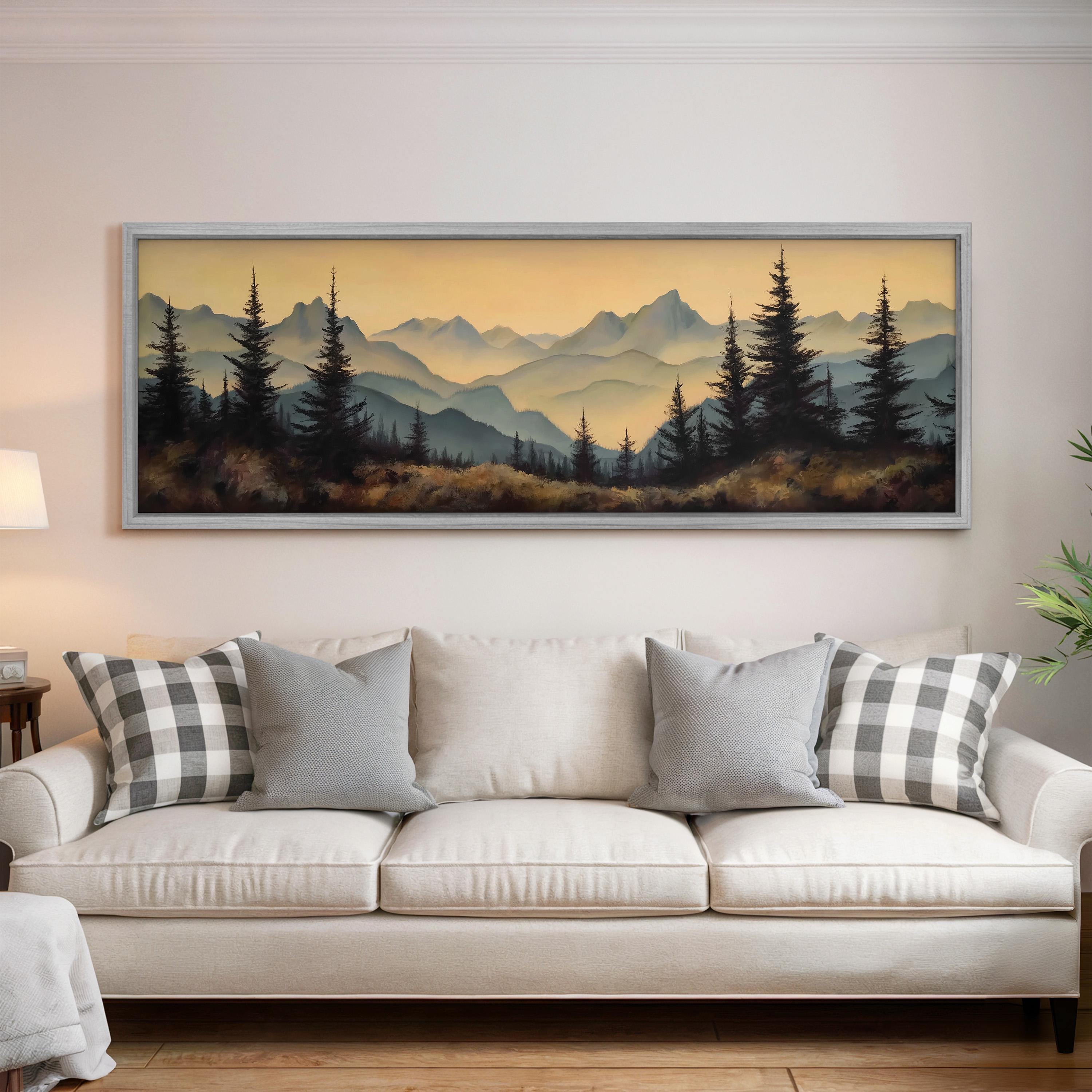 a large framed landscape painting hanging on a wall above a white sofa with gray and white patterned pillows.