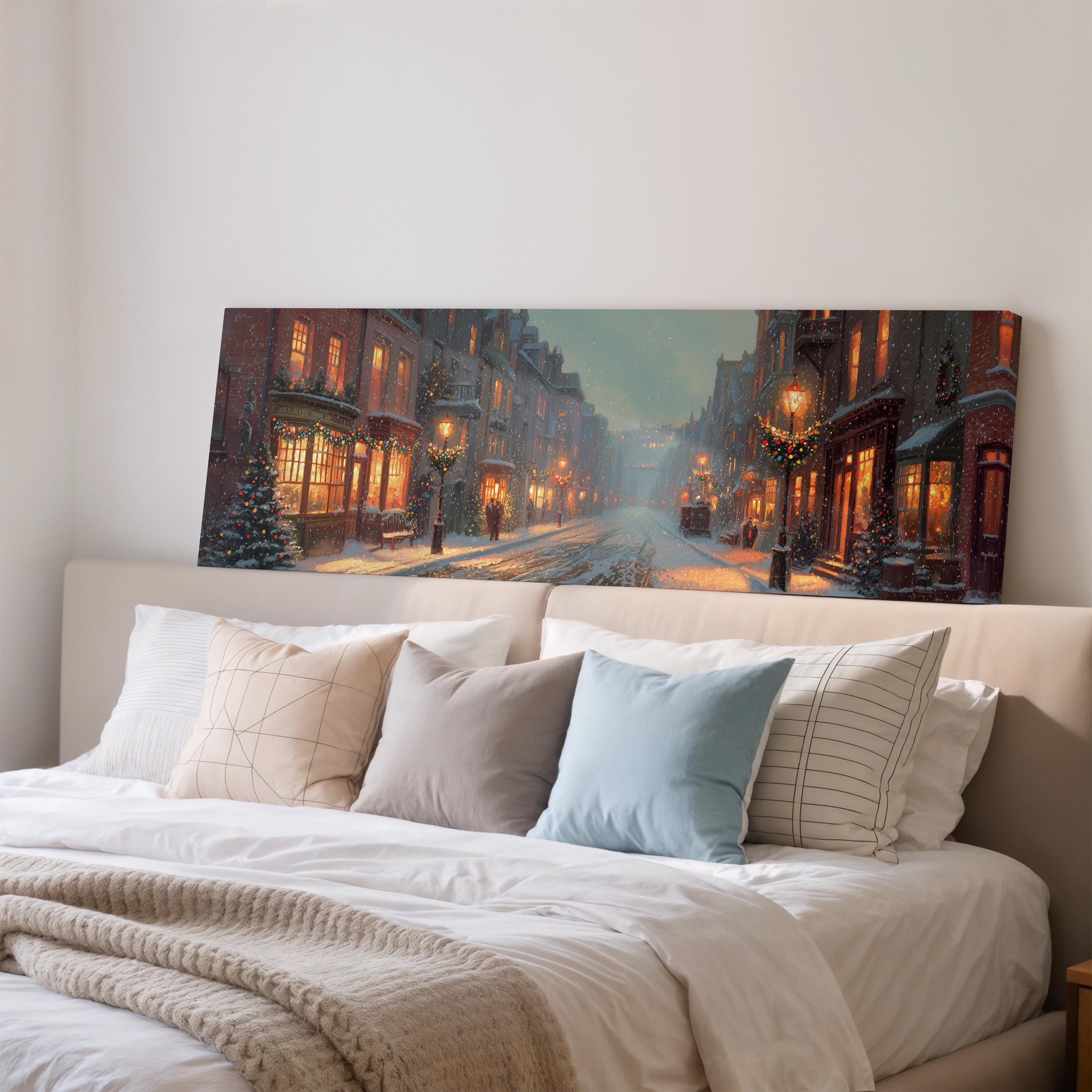 a large, colorful painting of a snowy city street with buildings, trees, and street lamps, hanging above a bed with white pillows and a gray blanket.