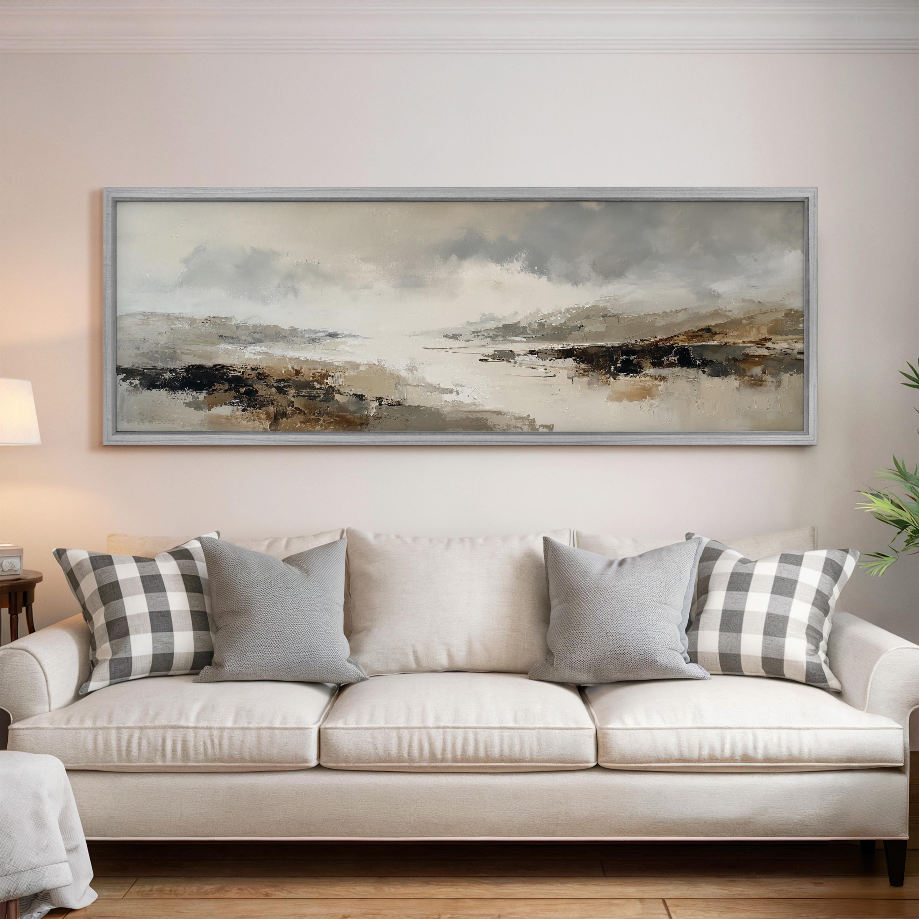 a large, framed landscape painting hanging on a wall above a white sofa with gray and white plaid throw pillows.