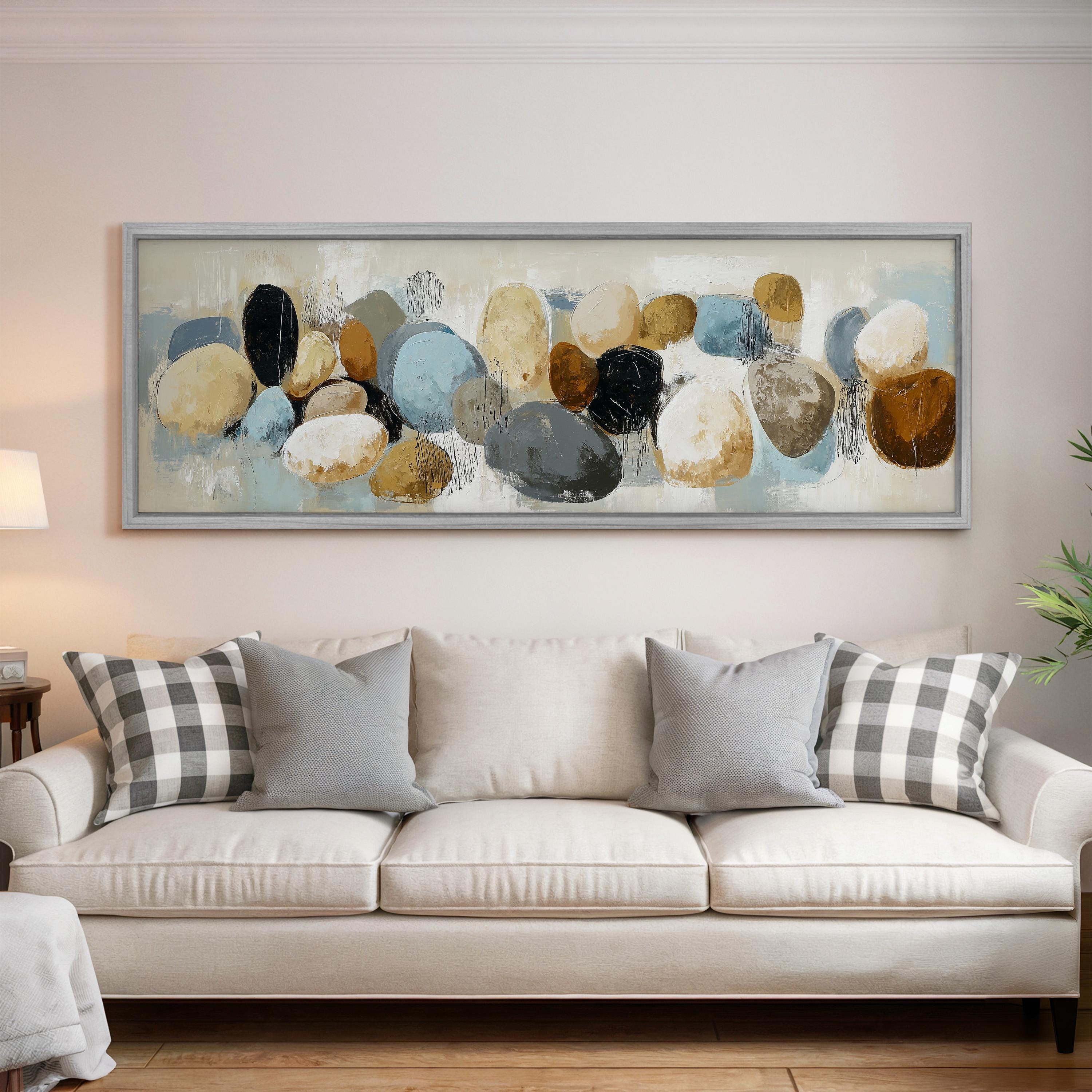 a large, abstract painting hanging on a wall above a white couch with gray and white plaid throw pillows.