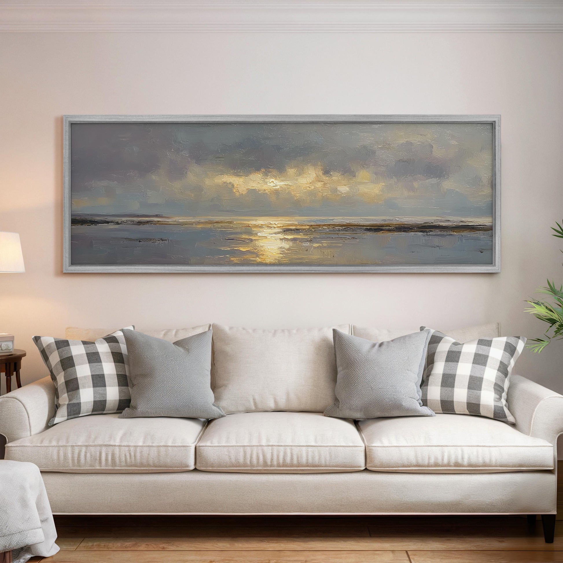 a large, framed painting of a serene landscape hanging on a wall above a white sofa with gray and white patterned throw pillows.