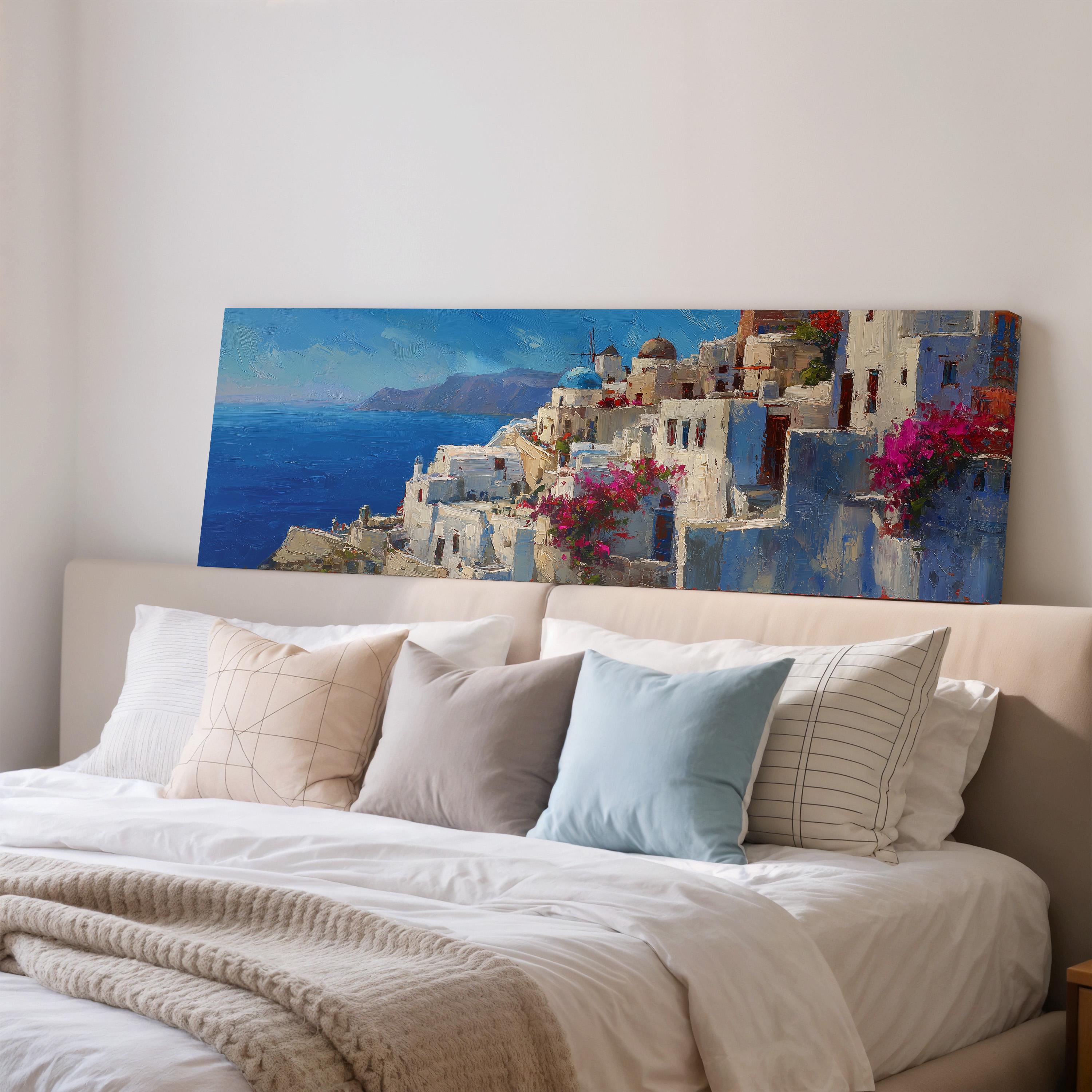 a large painting of a picturesque coastal town with white buildings, blue roofs, and pink flowers, hanging above a bed with white pillows and a gray blanket.