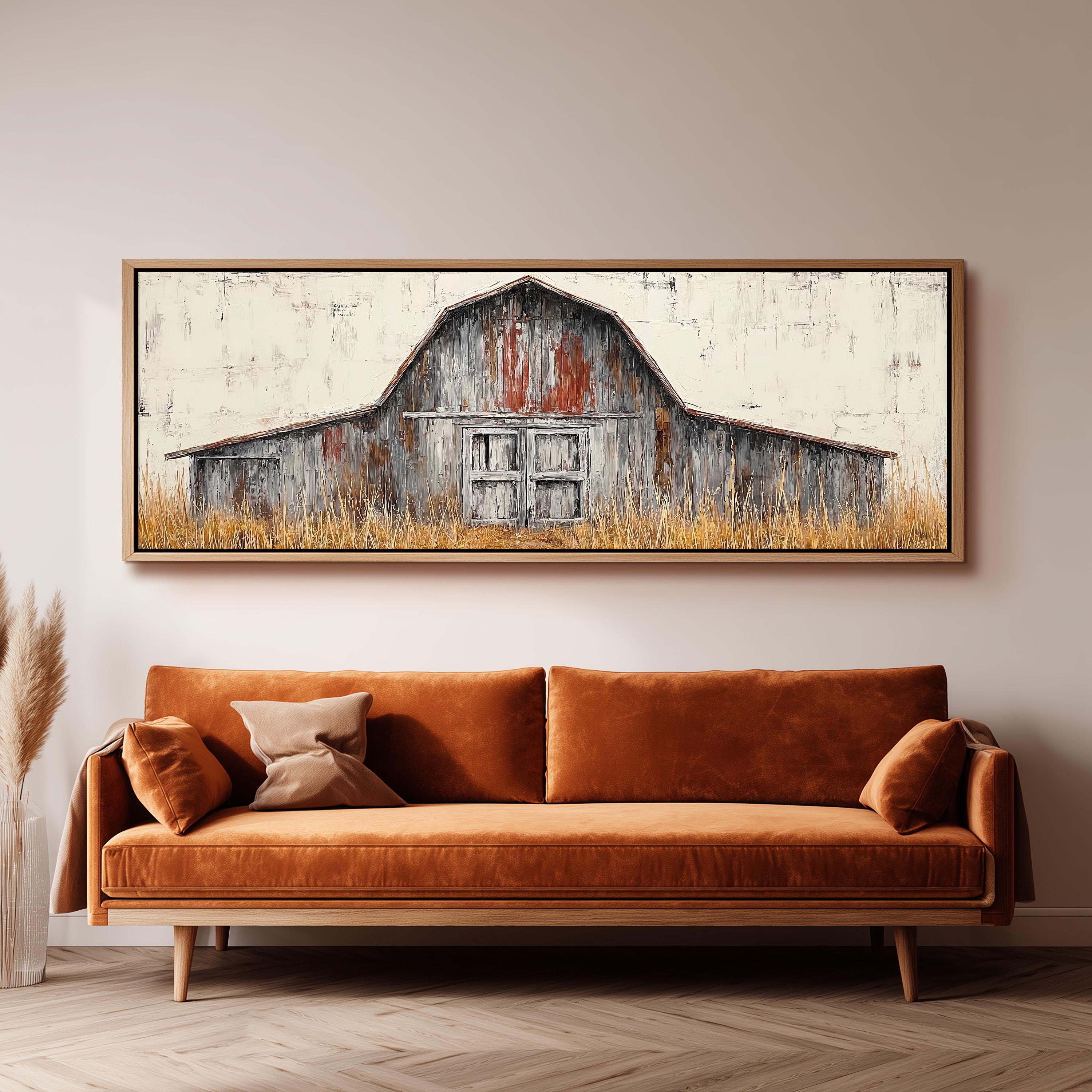 a large, rustic barn with a wooden door and window, set against a backdrop of tall grass. The barn is framed and hung on a wall above a brown sofa with a wooden frame.