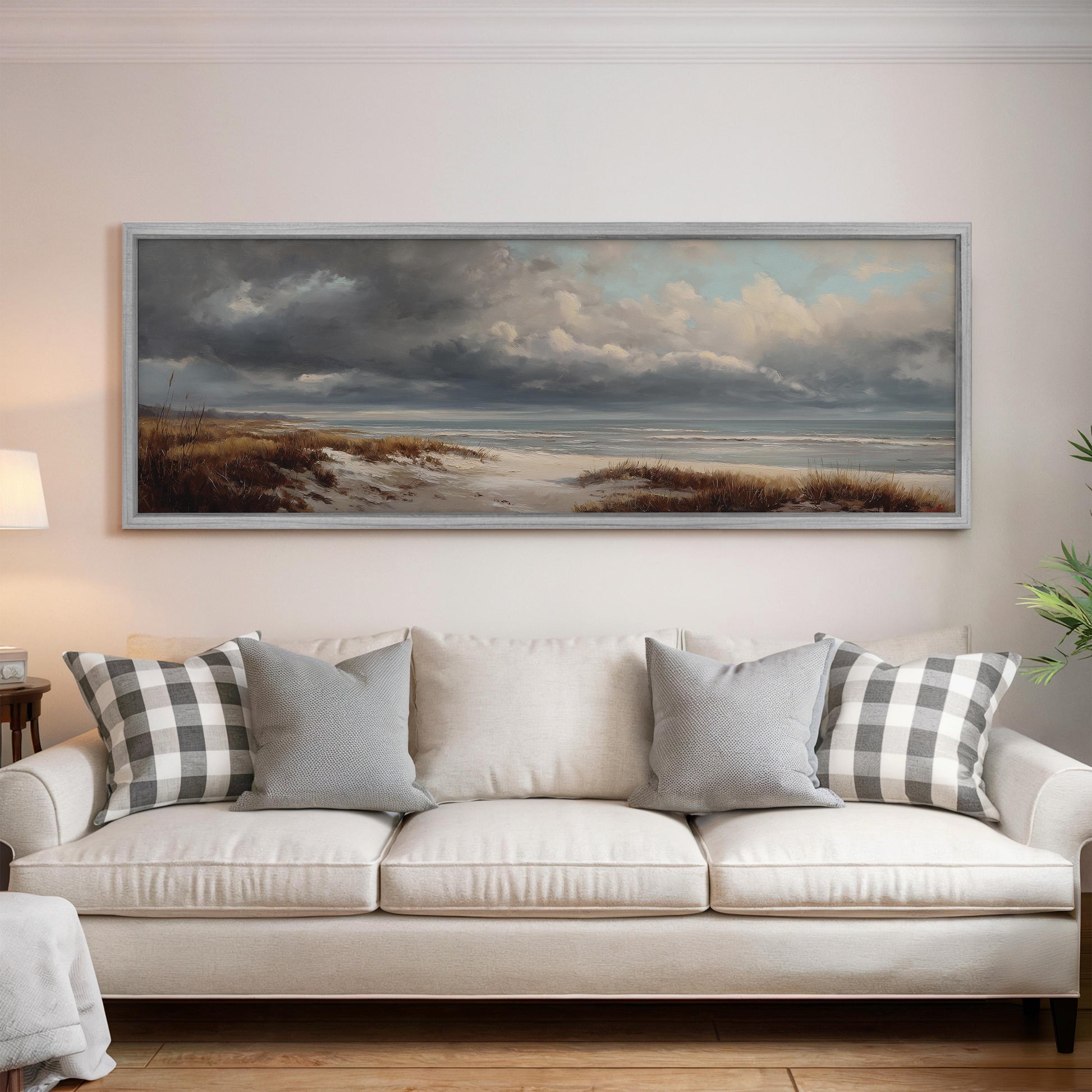 a large painting of a beach scene hanging on a wall above a white sofa with gray and white patterned pillows.