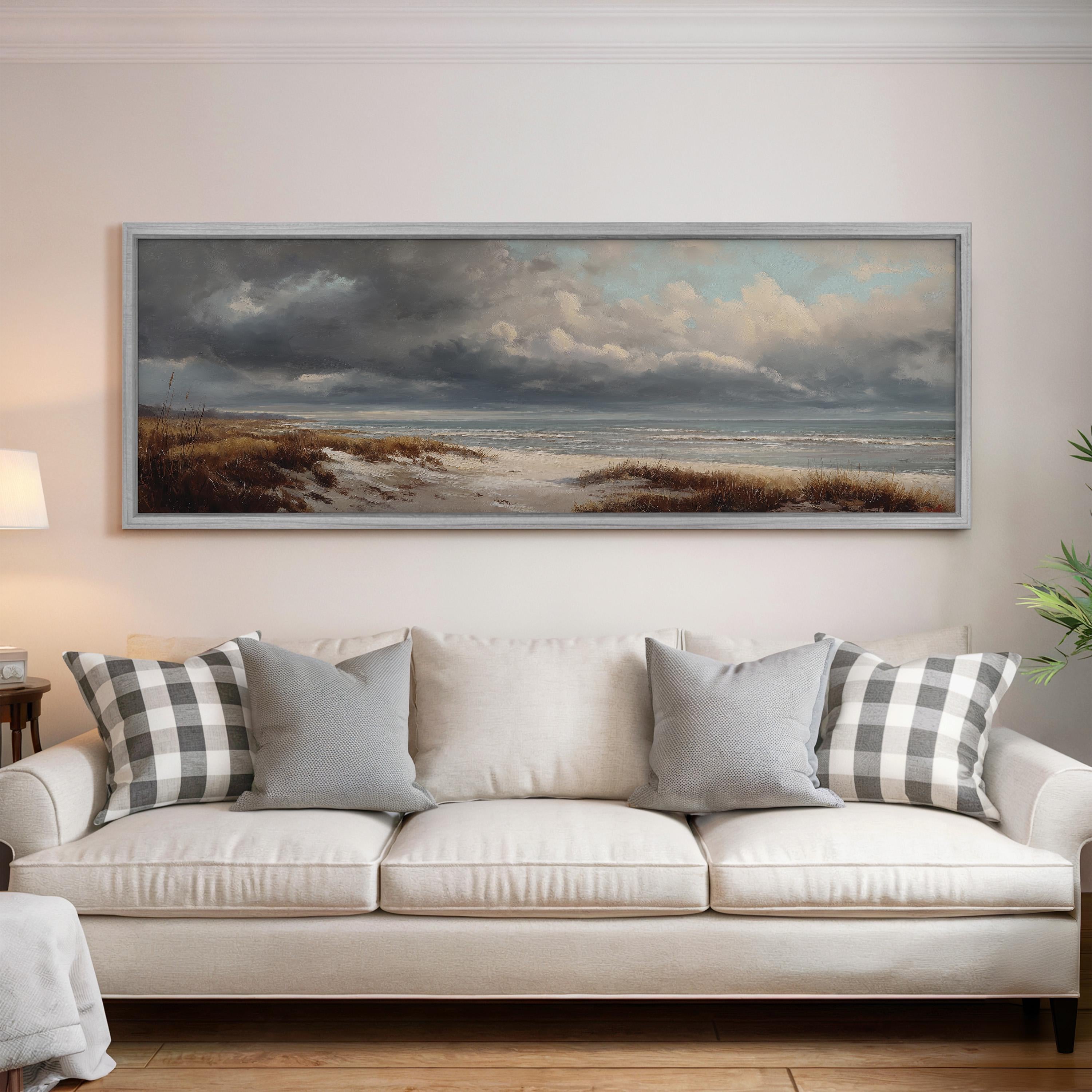 a large painting of a beach scene hanging on a wall above a white sofa with gray and white patterned pillows.