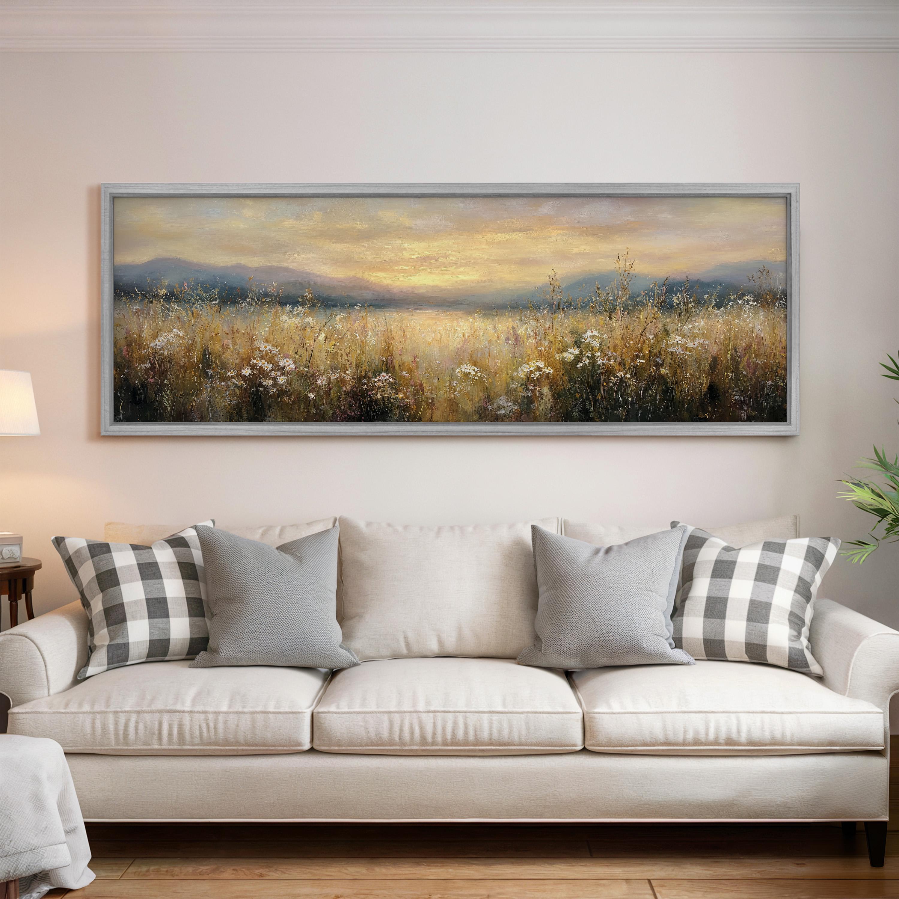 a large painting of a field with flowers hanging on a wall above a white sofa with gray and white pillows.