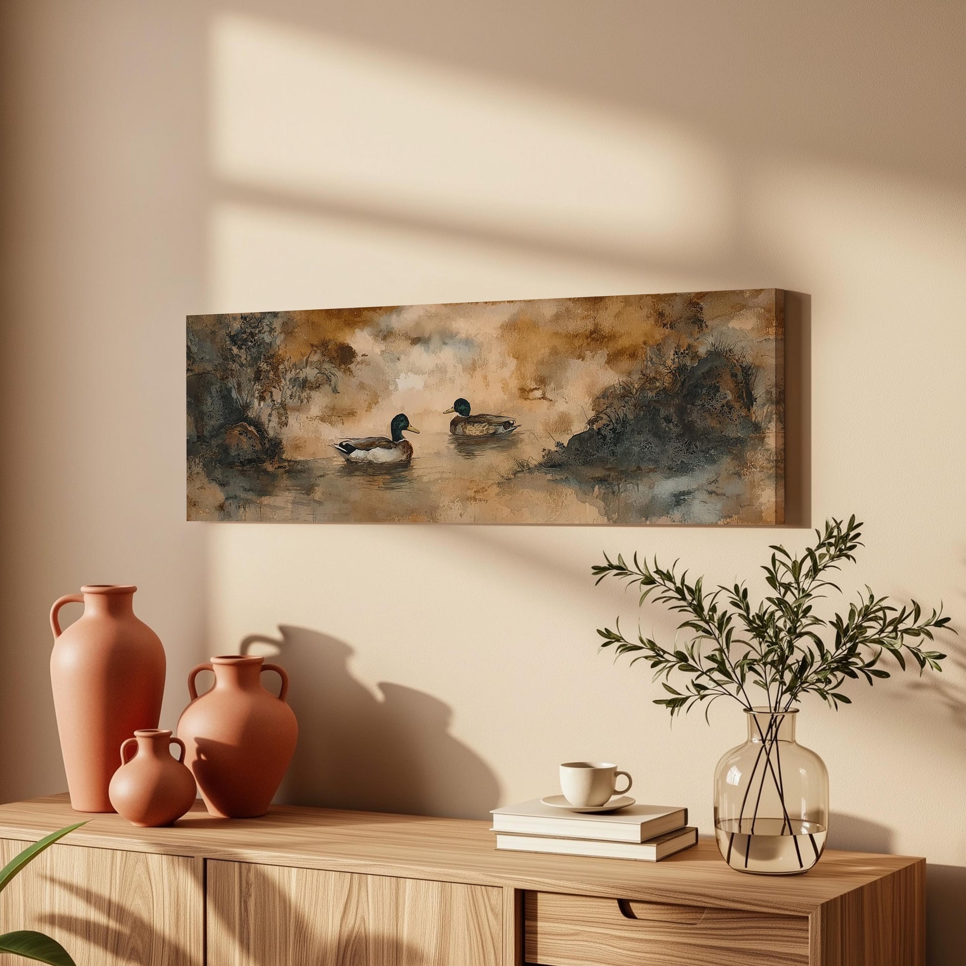 a wooden cabinet with a painting of ducks swimming in a pond hanging on the wall above it. The cabinet also has three orange vases, a white coffee cup, and a stack of books on top.