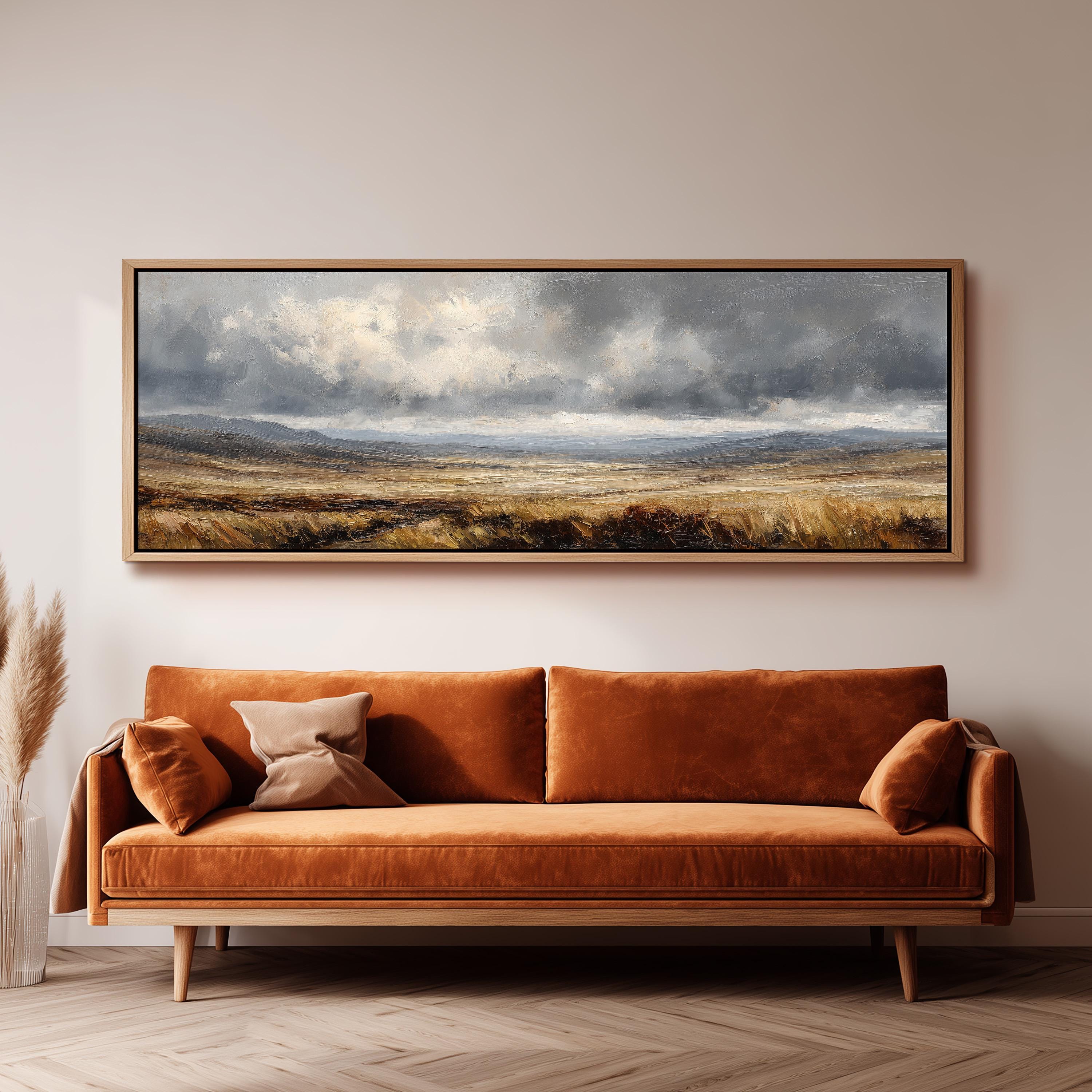 a large landscape painting hanging on a wall above a brown sofa with orange cushions.