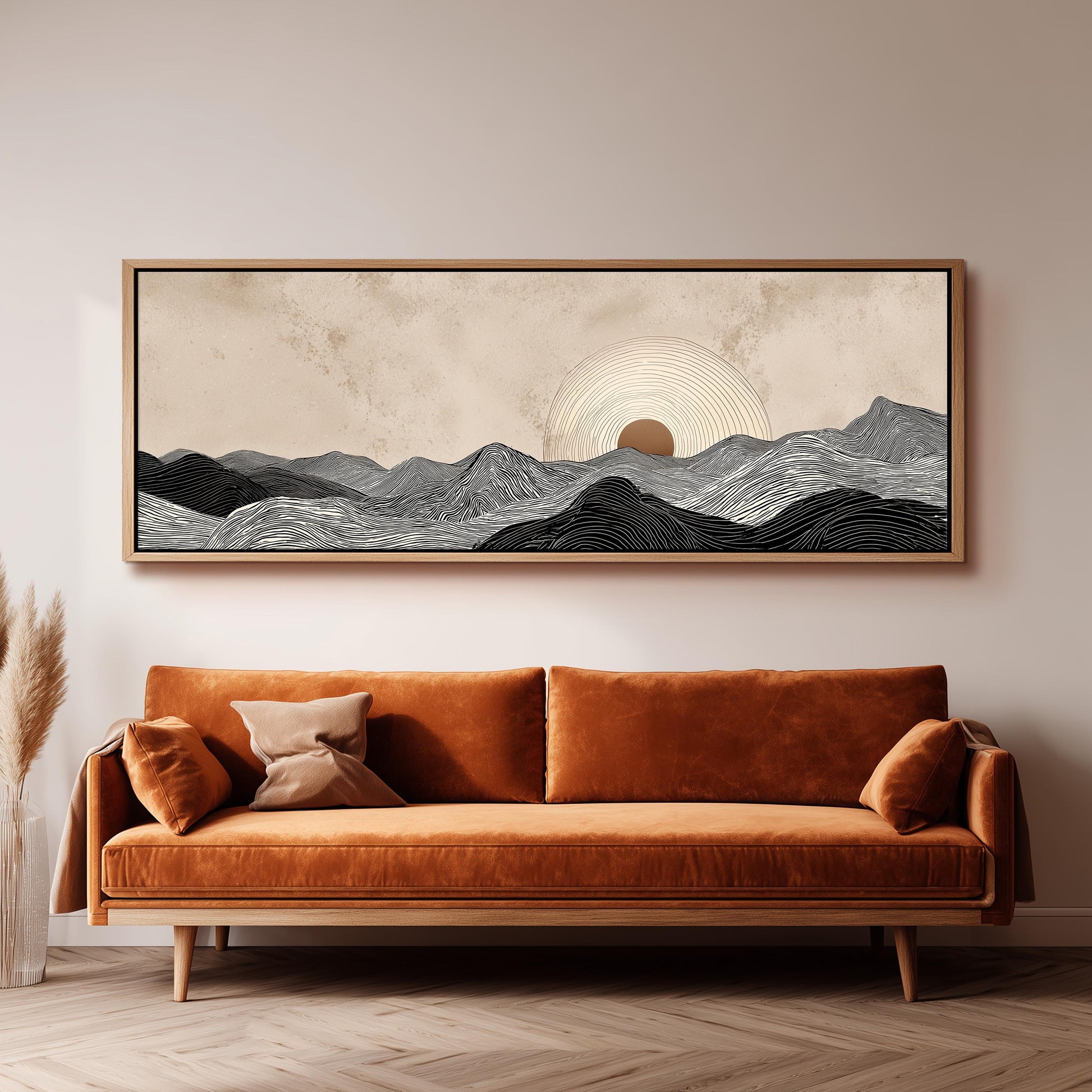 a large, framed artwork depicting a serene landscape with mountains and a sun in the sky, hanging above a brown sofa with orange cushions in a living room setting.