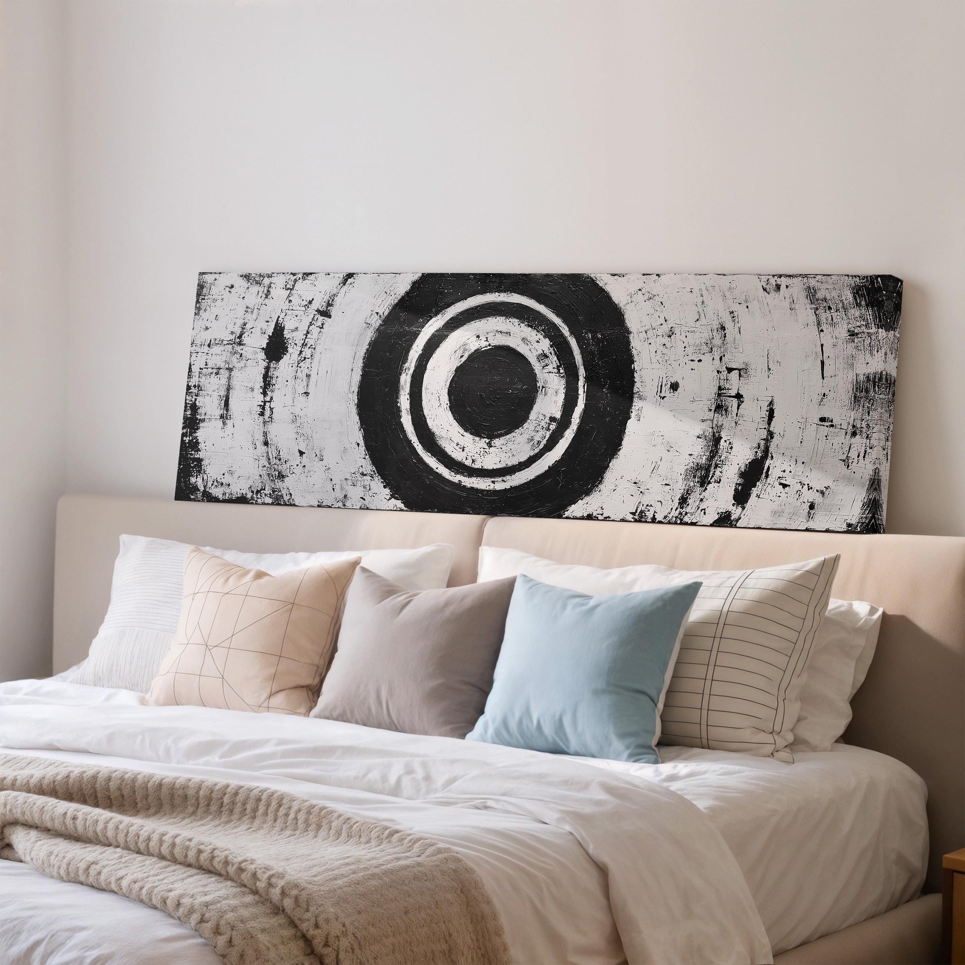a well-made bed with a large black and white circular artwork hanging above it.