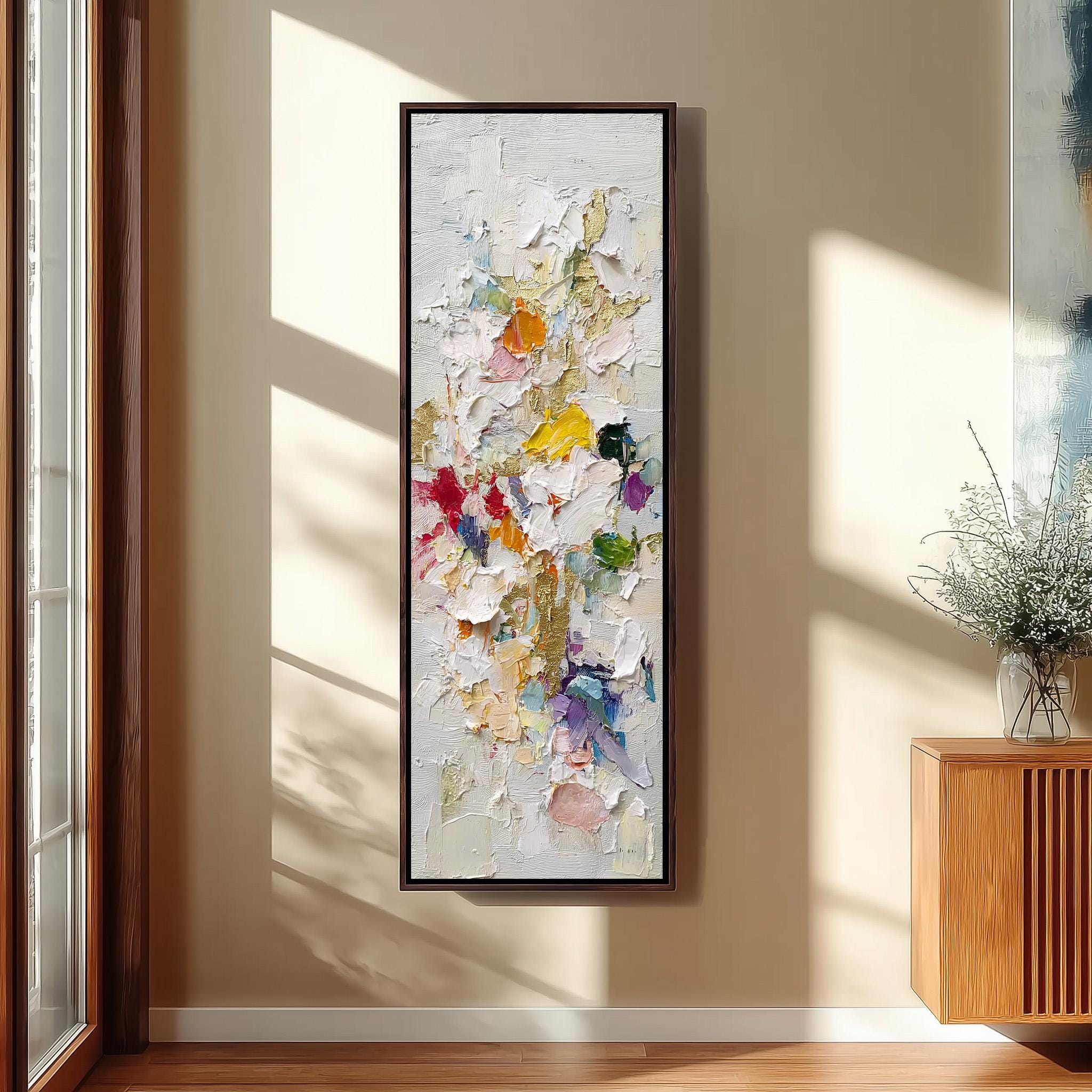 a large, colorful painting hanging on a wall in a room with a wooden cabinet and a vase of flowers.