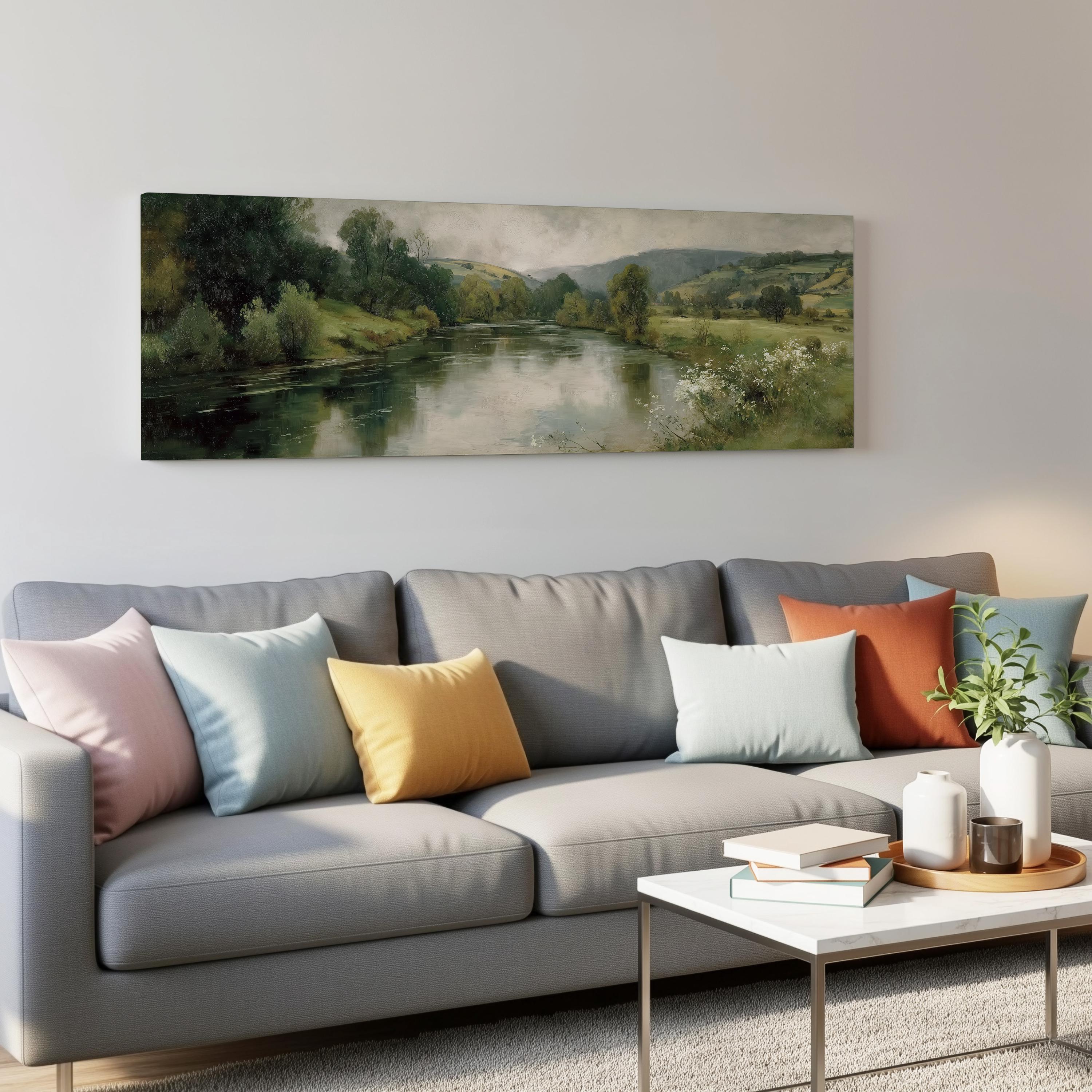 a living room with a gray sofa adorned with colorful throw pillows, a coffee table with books and a plant, and a large landscape painting hanging on the wall above the sofa.