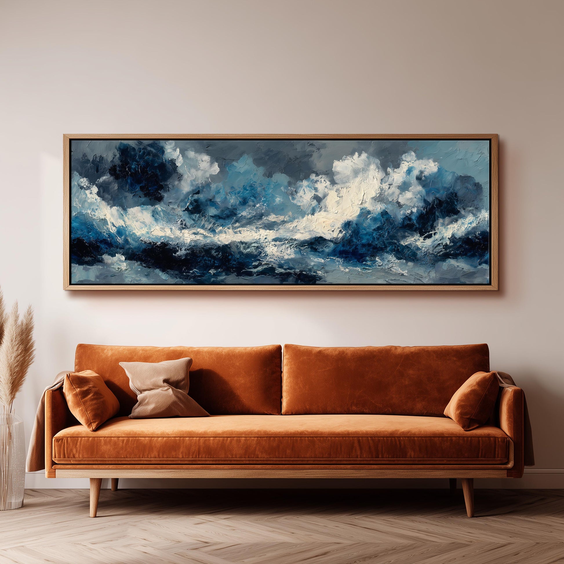 a large, framed painting of a stormy ocean scene hanging on a wall above a brown sofa.