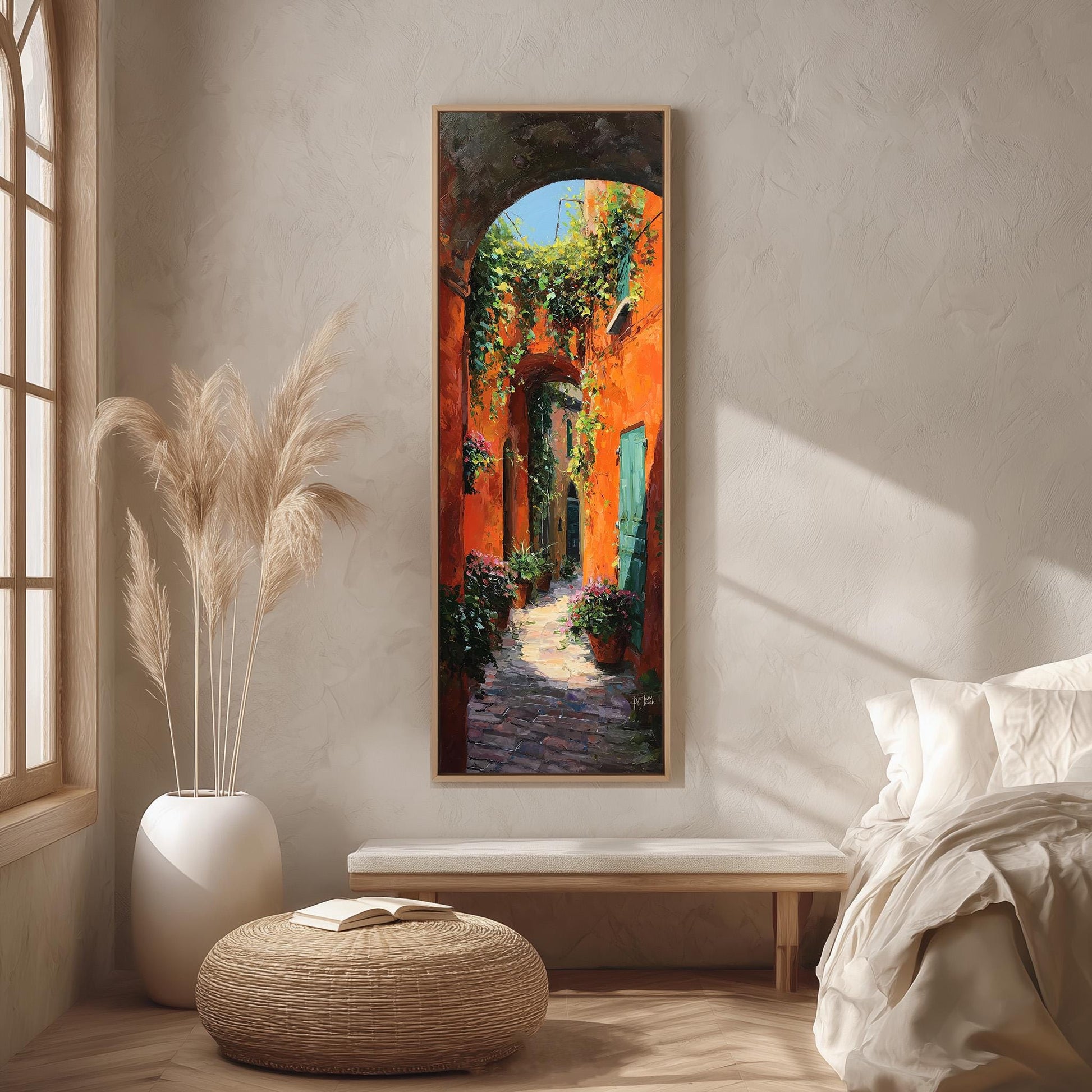 a large painting of a colorful alleyway with a red brick path, surrounded by greenery and flowers, hanging on a wall in a room with a bed, a potted plant, and a woven ottoman.