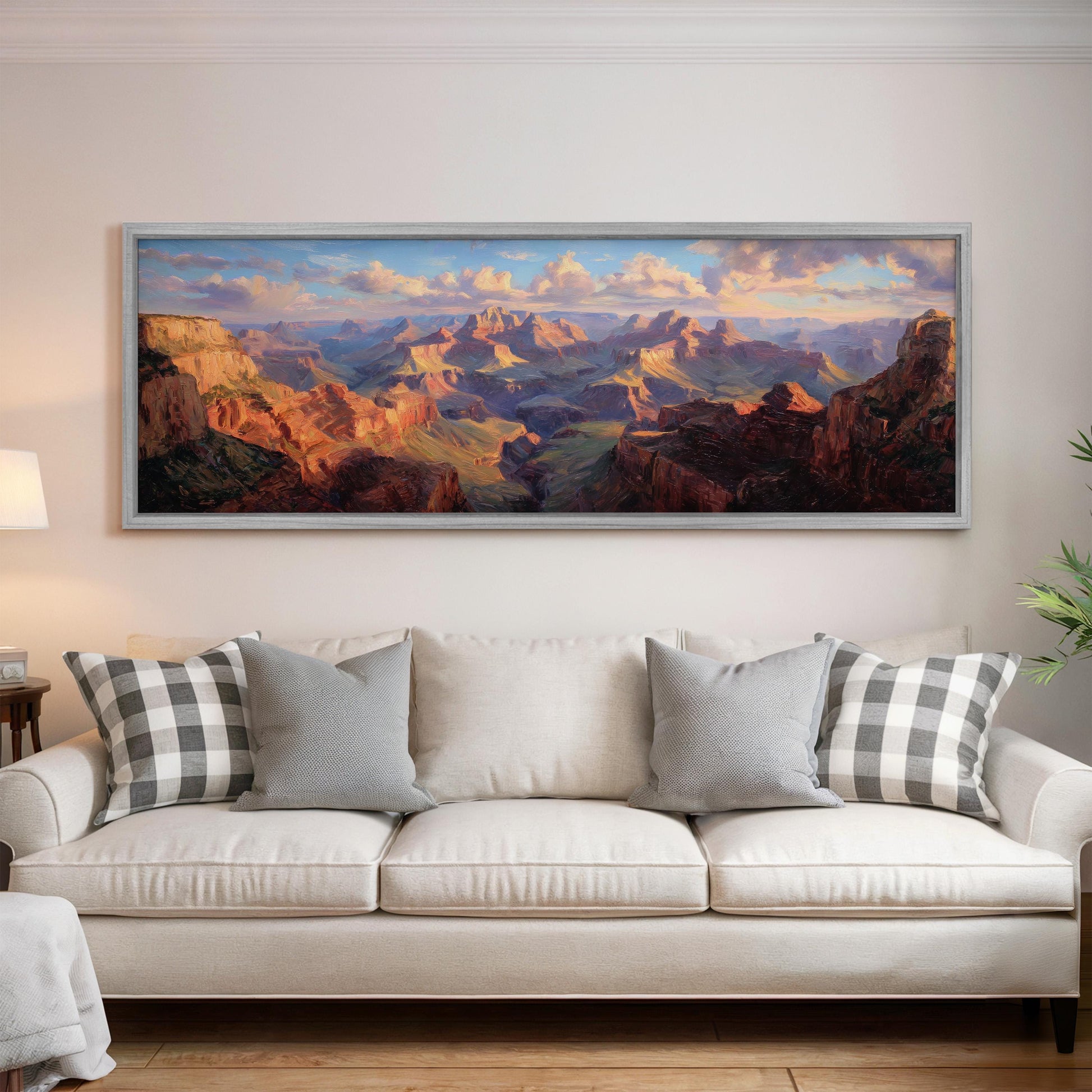 a large, framed painting of a scenic mountain landscape hanging on a wall above a white couch with patterned throw pillows.