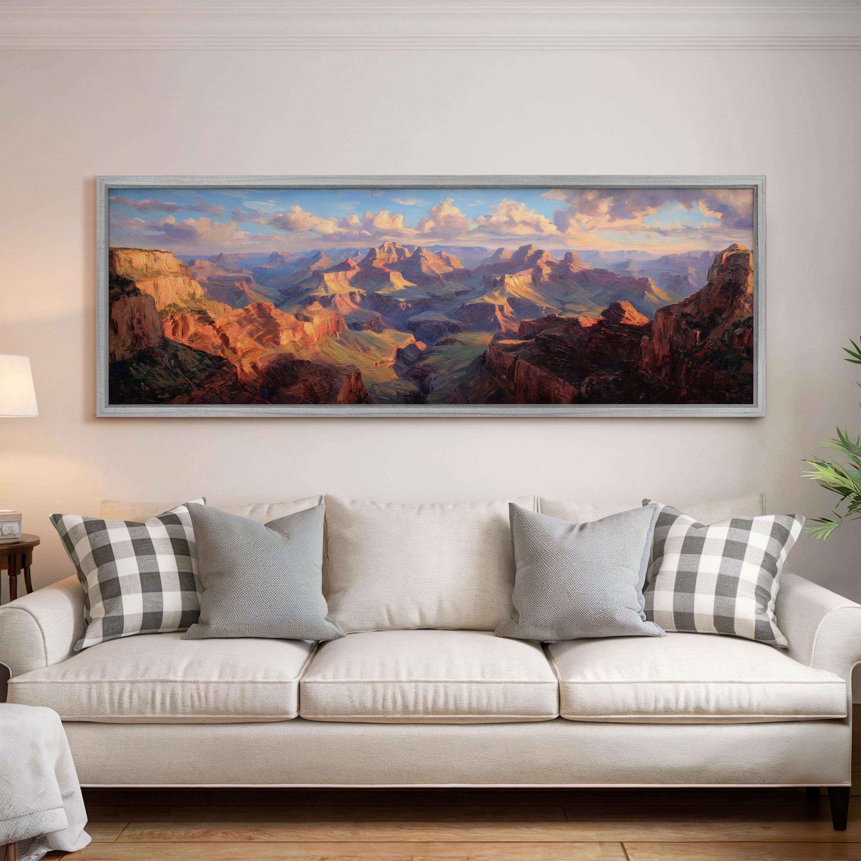 a large, framed painting of a scenic mountain landscape hanging on a wall above a white couch with patterned throw pillows.