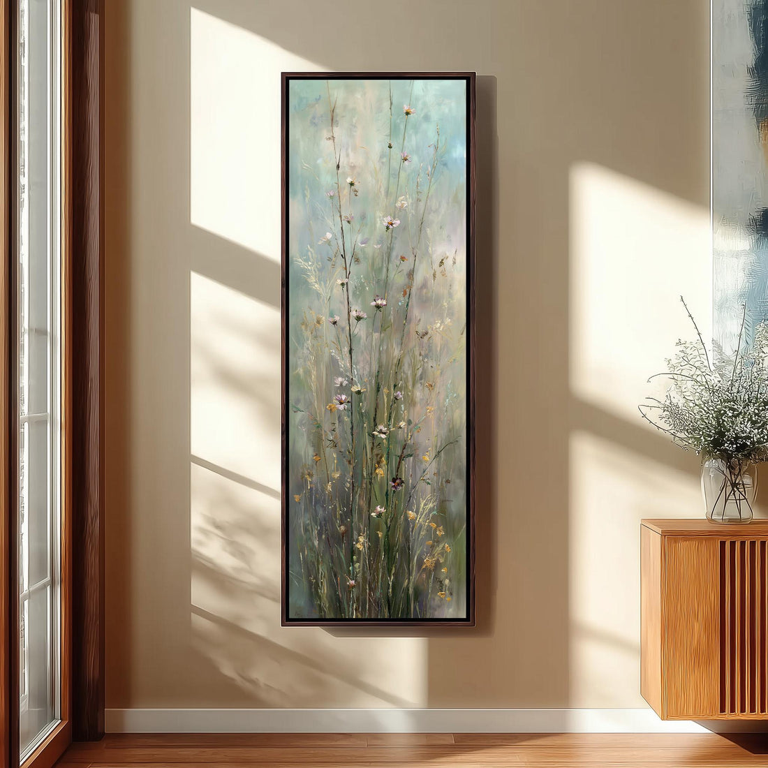 a large painting of tall grasses with flowers hanging on a wall in a room with a wooden chair, a small table, and a window.