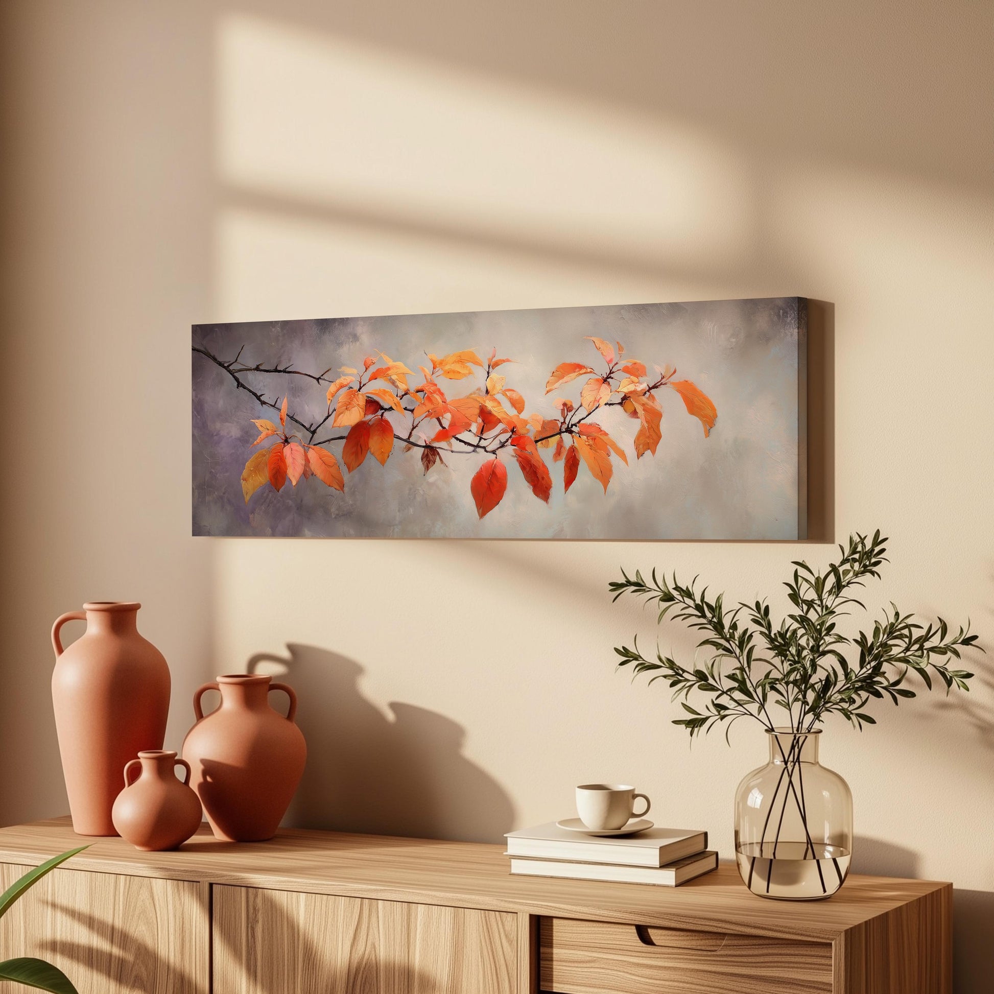 a wooden cabinet with a vase, a plant, and a stack of books on top. Above the cabinet, there is a painting of orange leaves hanging on the wall.