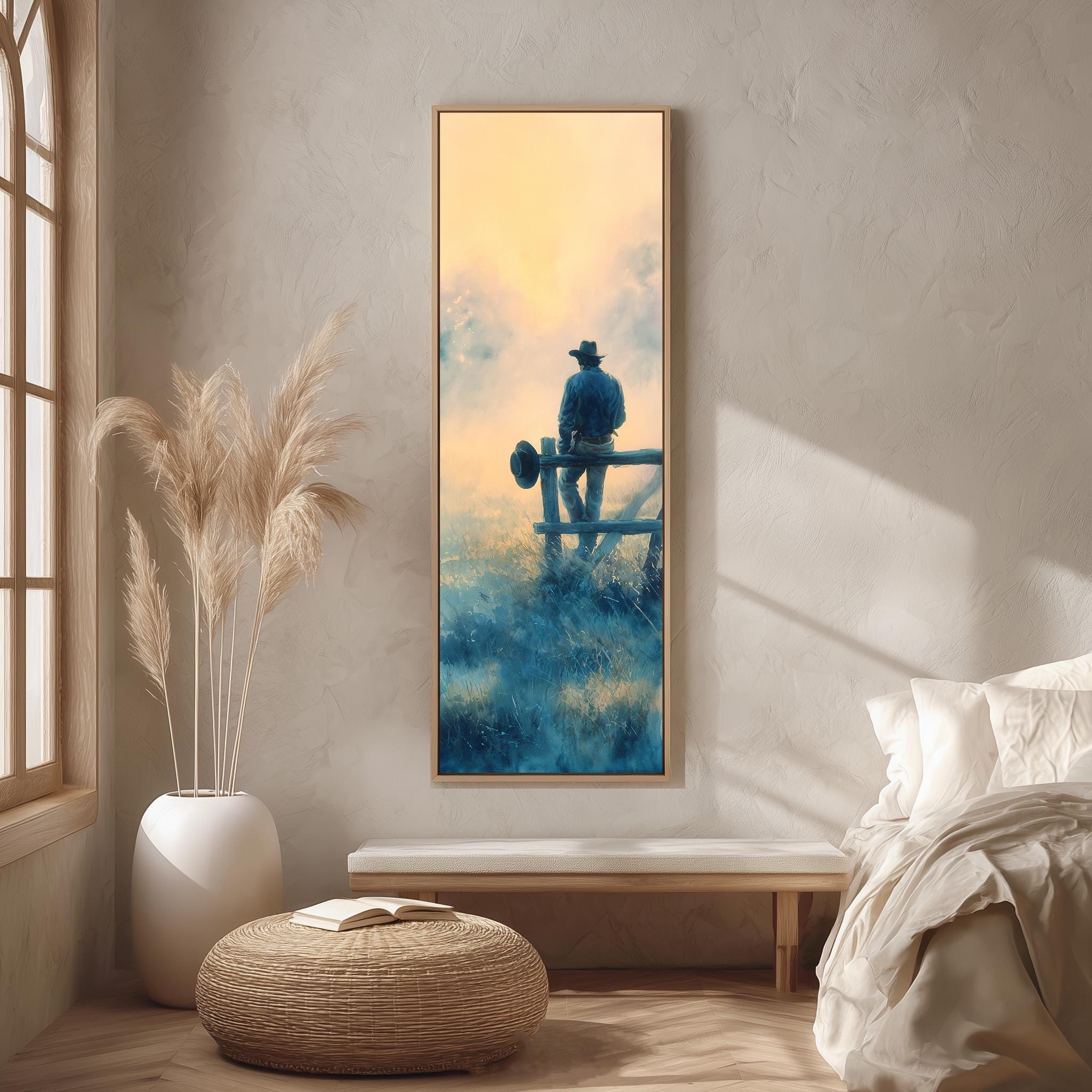 a serene indoor setting with a large painting of a cowboy sitting on a fence, surrounded by a peaceful landscape. The painting is hung on a wall, and the room features a bed, a potted plant, and a woven ottoman.