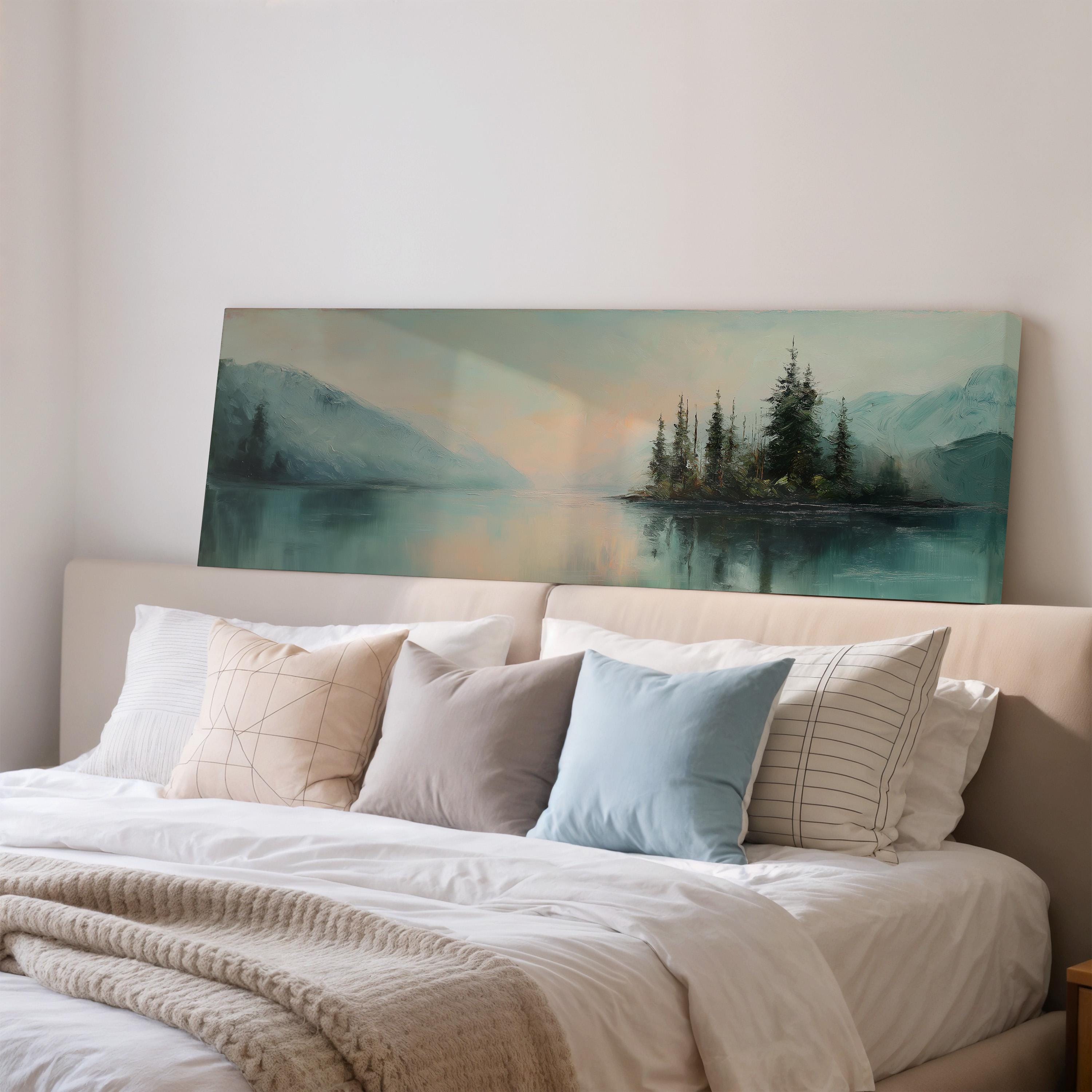 a large painting of a serene landscape with a lake and mountains in the background, hanging above a bed with white pillows and a gray blanket.