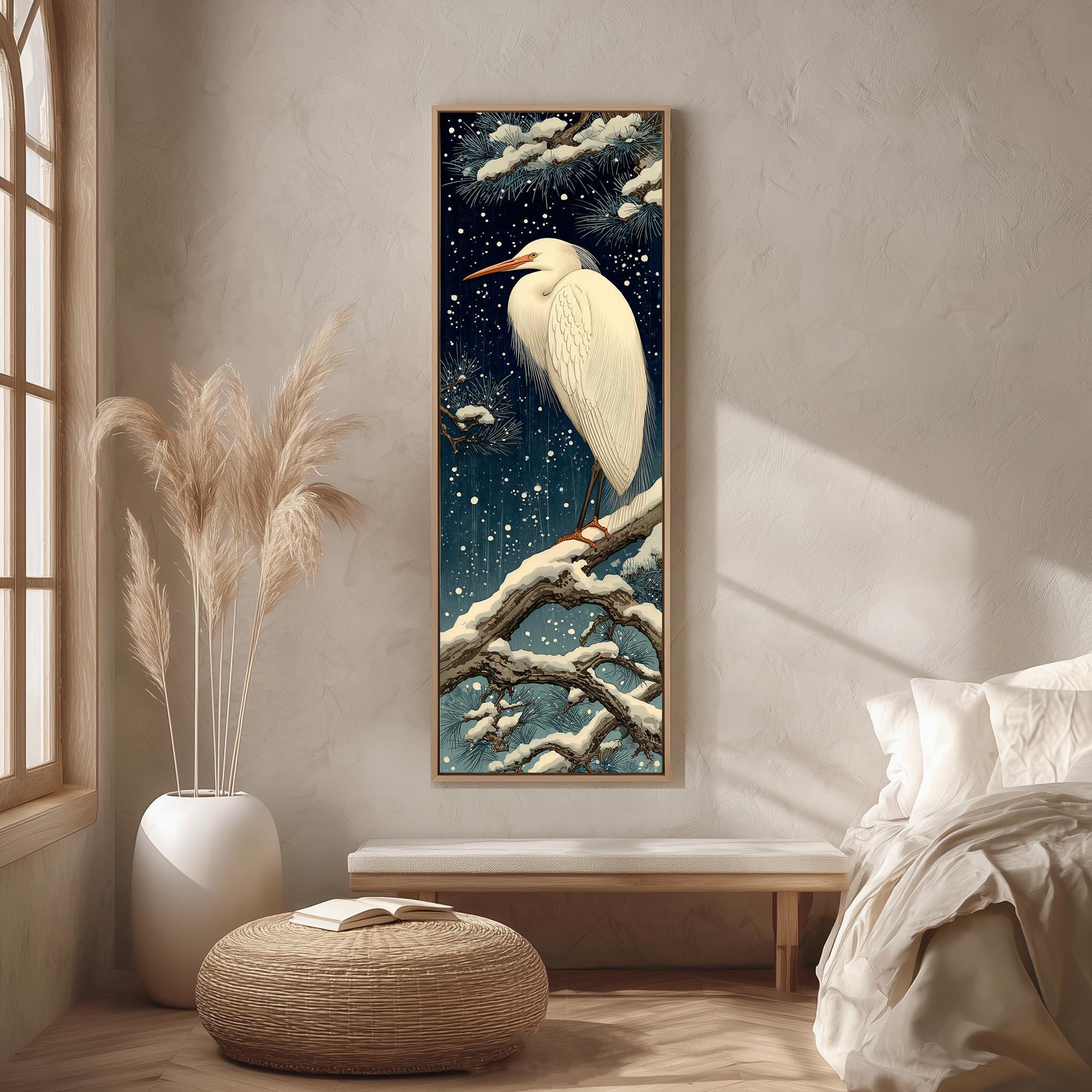 a large, framed painting of a white heron perched on a branch, set against a night sky with stars. The painting is hung on a wall in a room with a bed, a potted plant, and a woven ottoman.