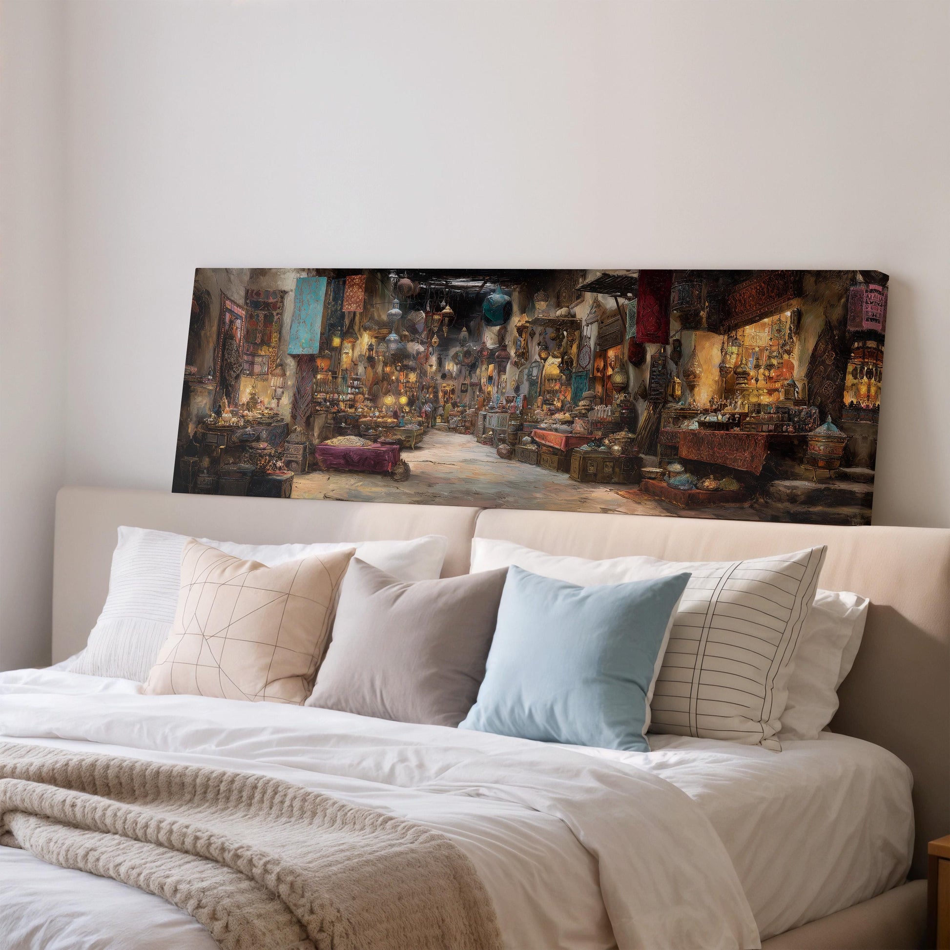 a large painting of a bustling market scene hanging on a wall above a bed with white pillows and a gray blanket.