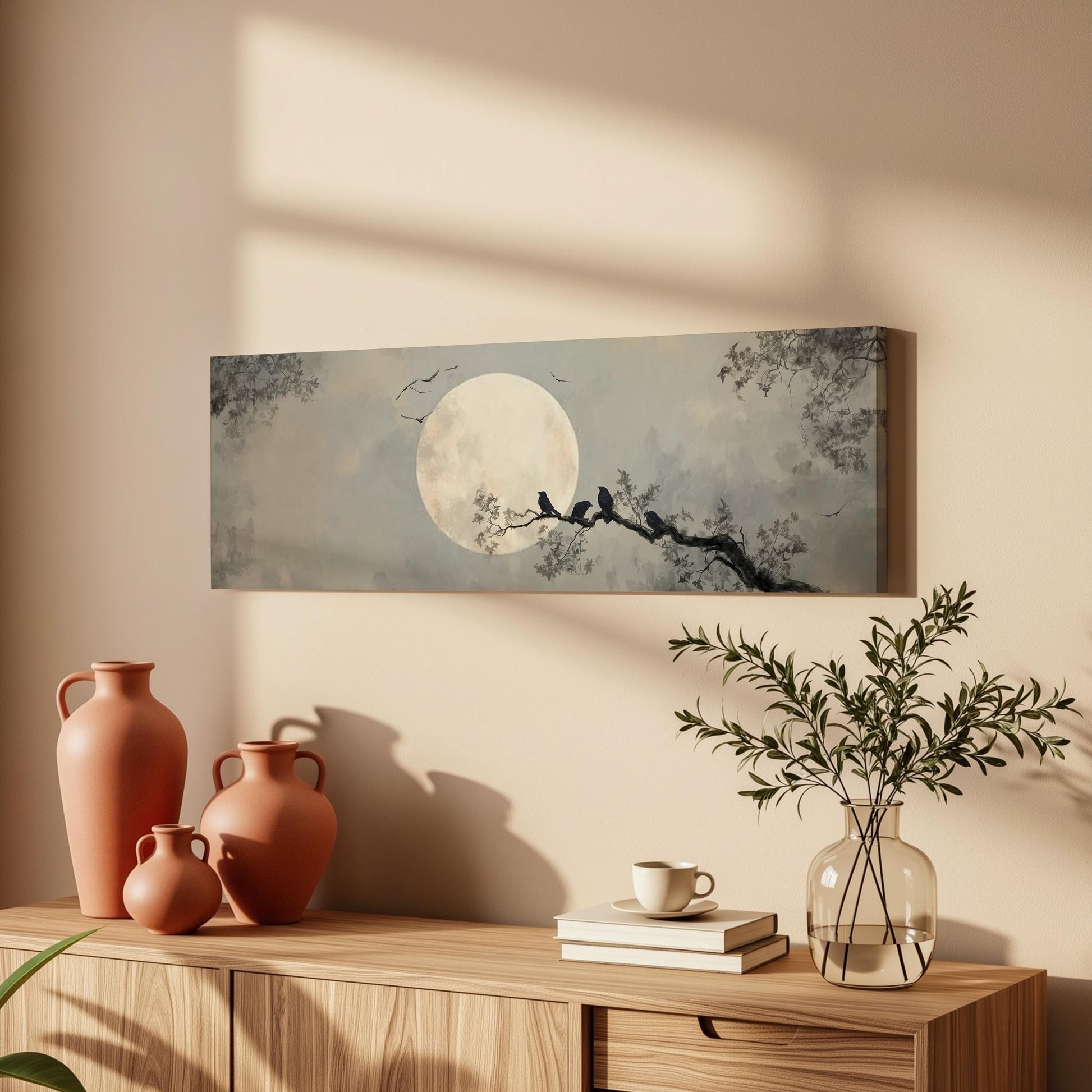 a wooden cabinet with a vase, a plant, and a book on top of it, along with a framed painting of a moonlit tree branch with birds perched on it.