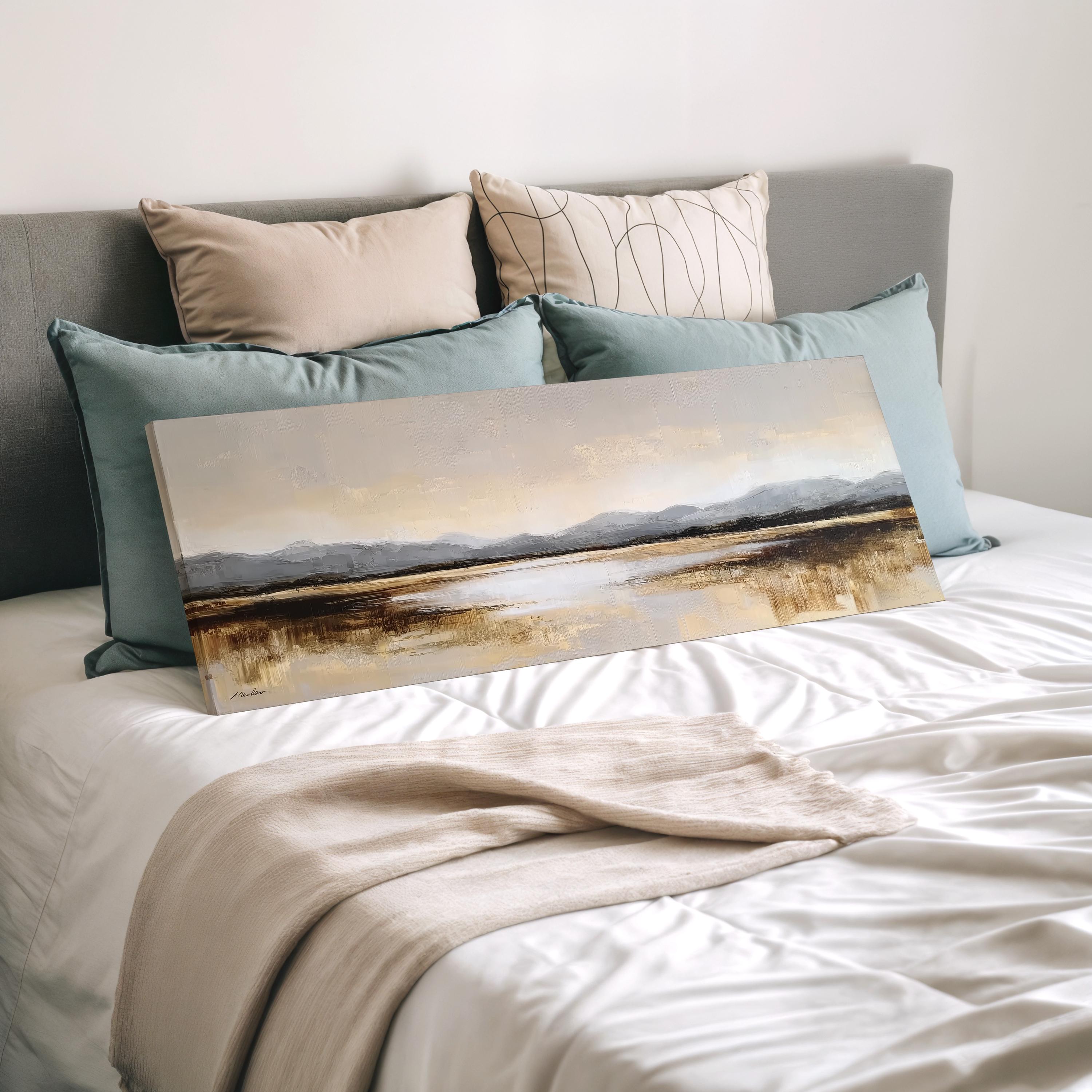 a bedroom with a bed and a painting of a landscape on it. The bed has a white comforter and is adorned with several pillows in various colors. The painting is placed on the bed, creating a cozy and inviting atmosphere.