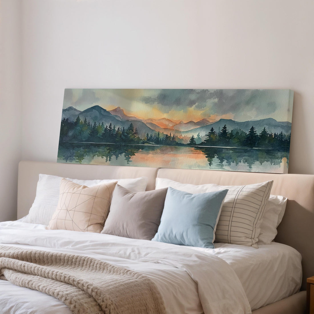a large, framed painting of a serene landscape with mountains, trees, and a lake, hanging on a wall above a brown sofa.