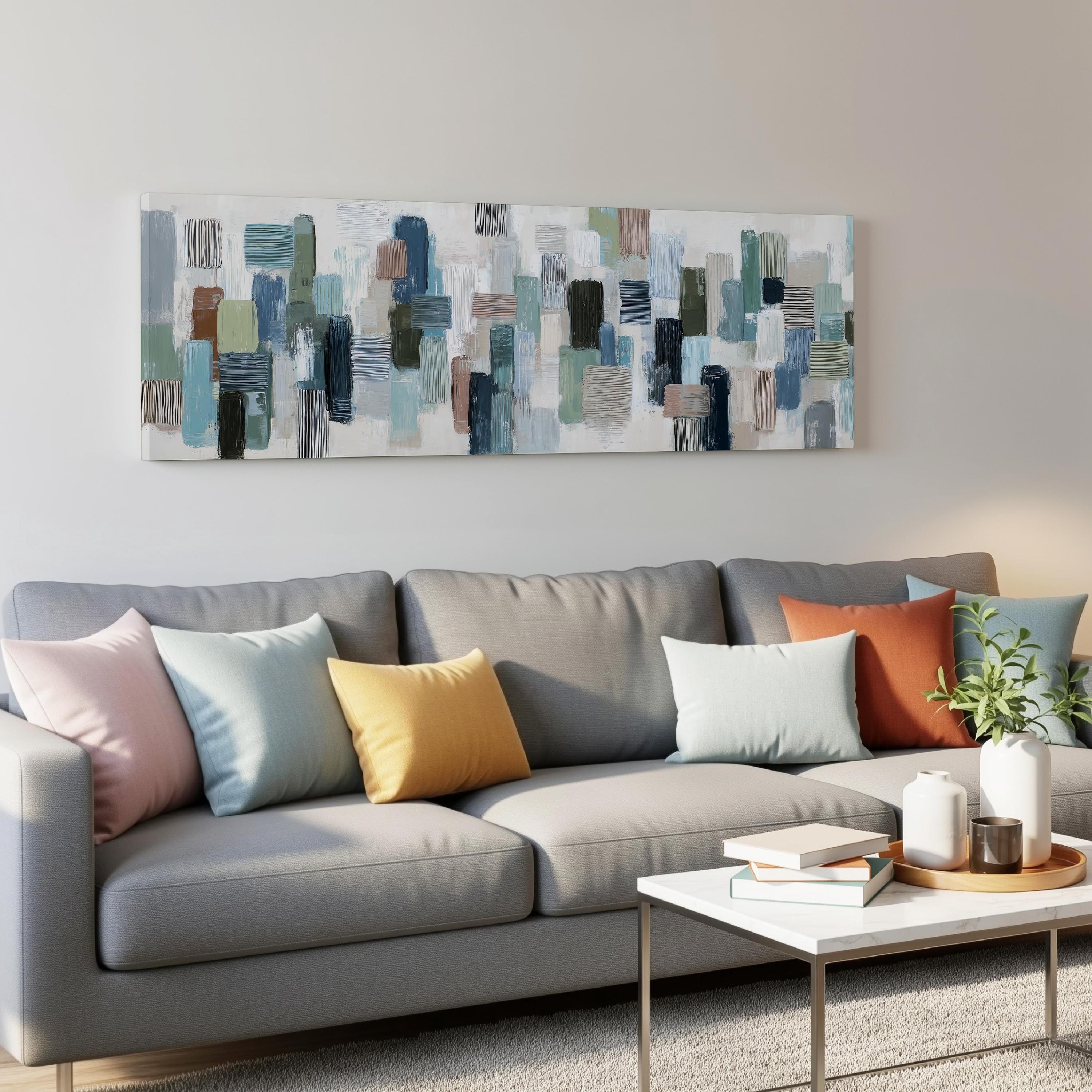 a modern living room with a gray sofa adorned with colorful throw pillows. Above the sofa, there is a large abstract painting on the wall. In front of the sofa, there is a white coffee table with a stack of books and a small plant.