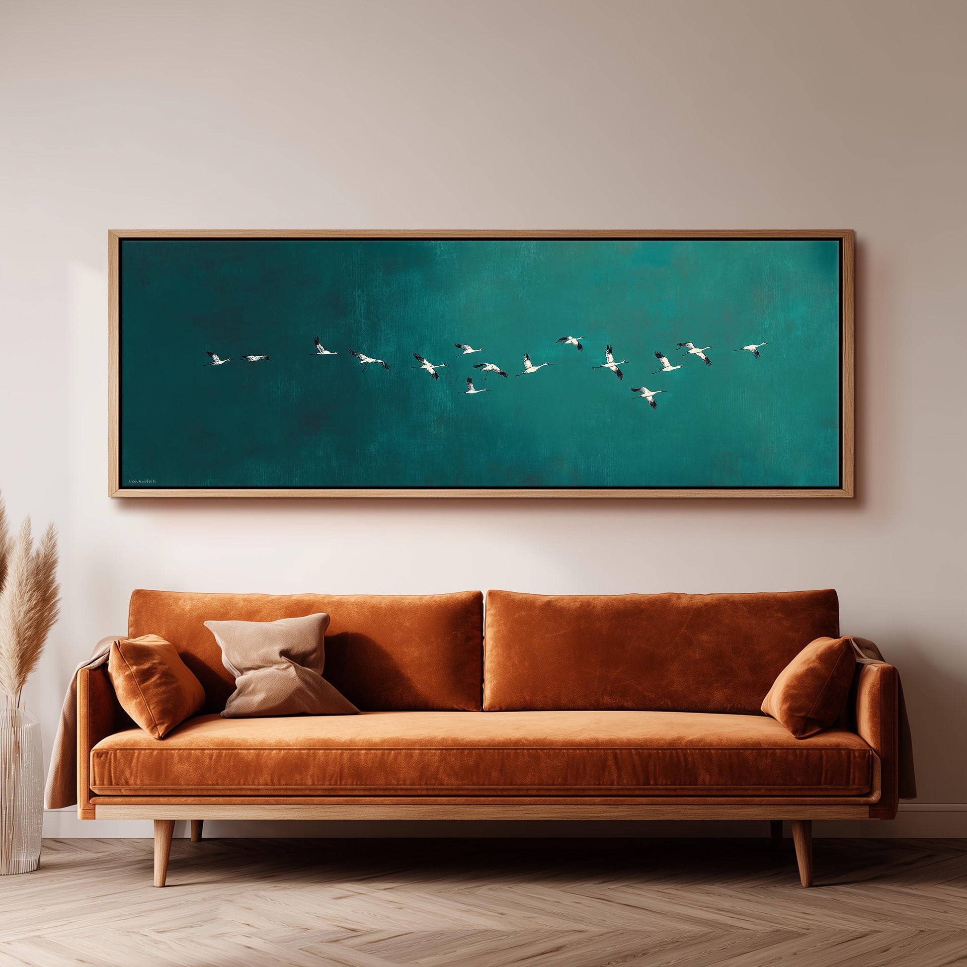 a large, framed painting of a flock of birds flying over a green background, hanging on a wall above a brown sofa.
