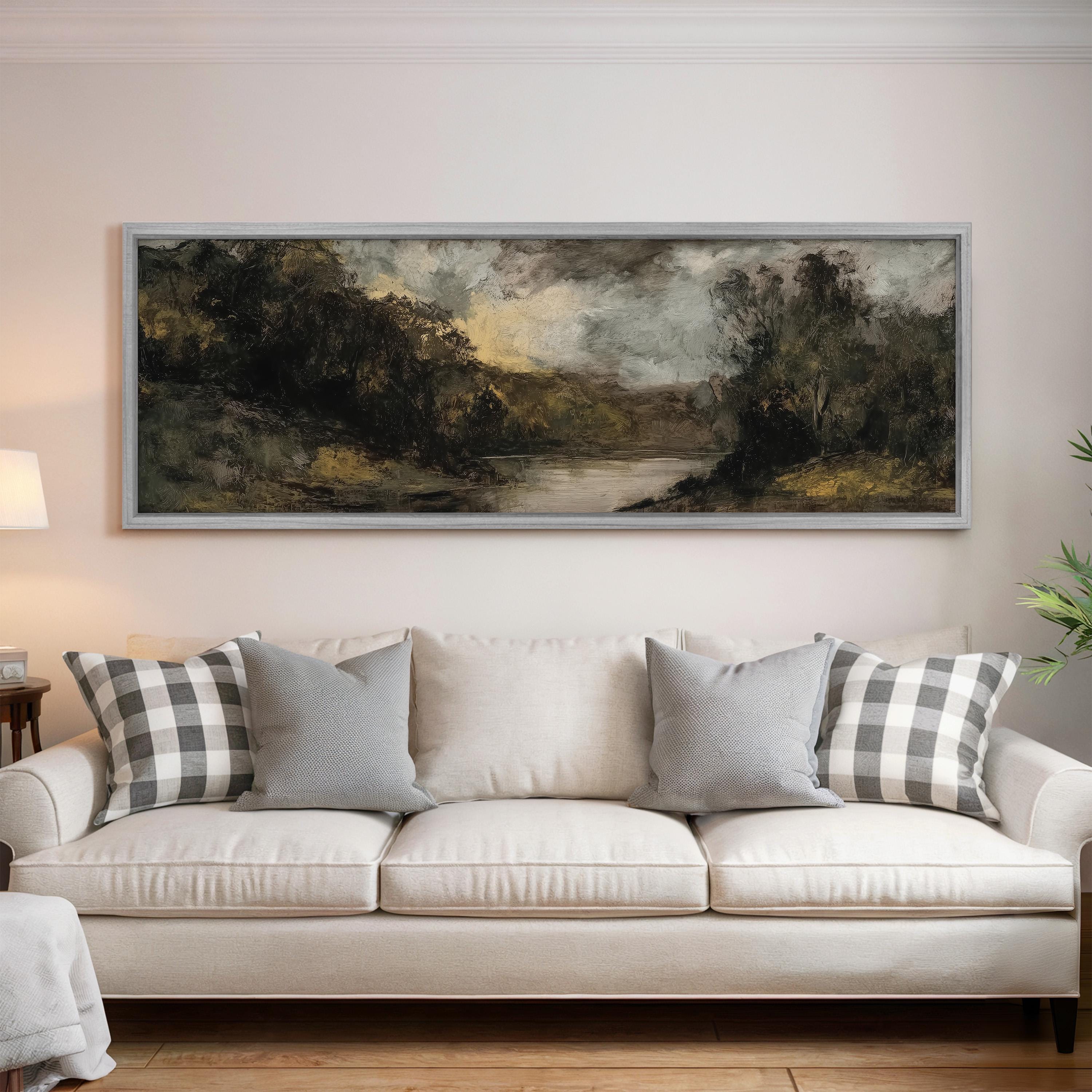 a large landscape painting hanging on a wall above a white sofa with gray and white plaid throw pillows.