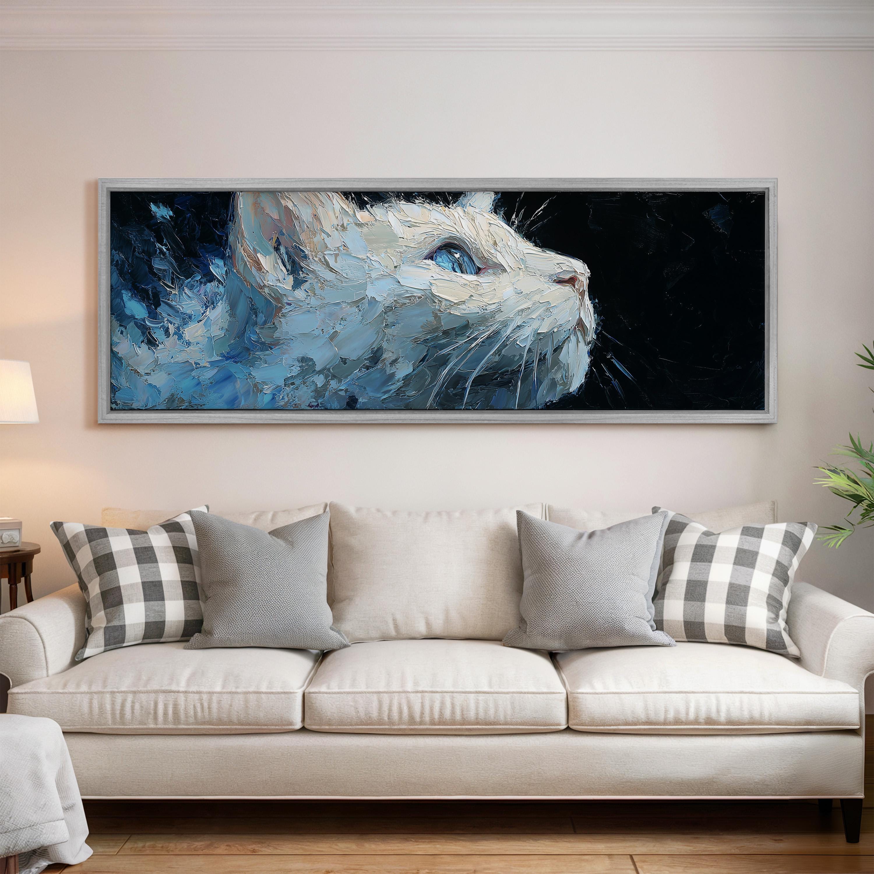 a large, framed painting of a cat's face hanging on a wall above a white couch with gray and white plaid throw pillows.