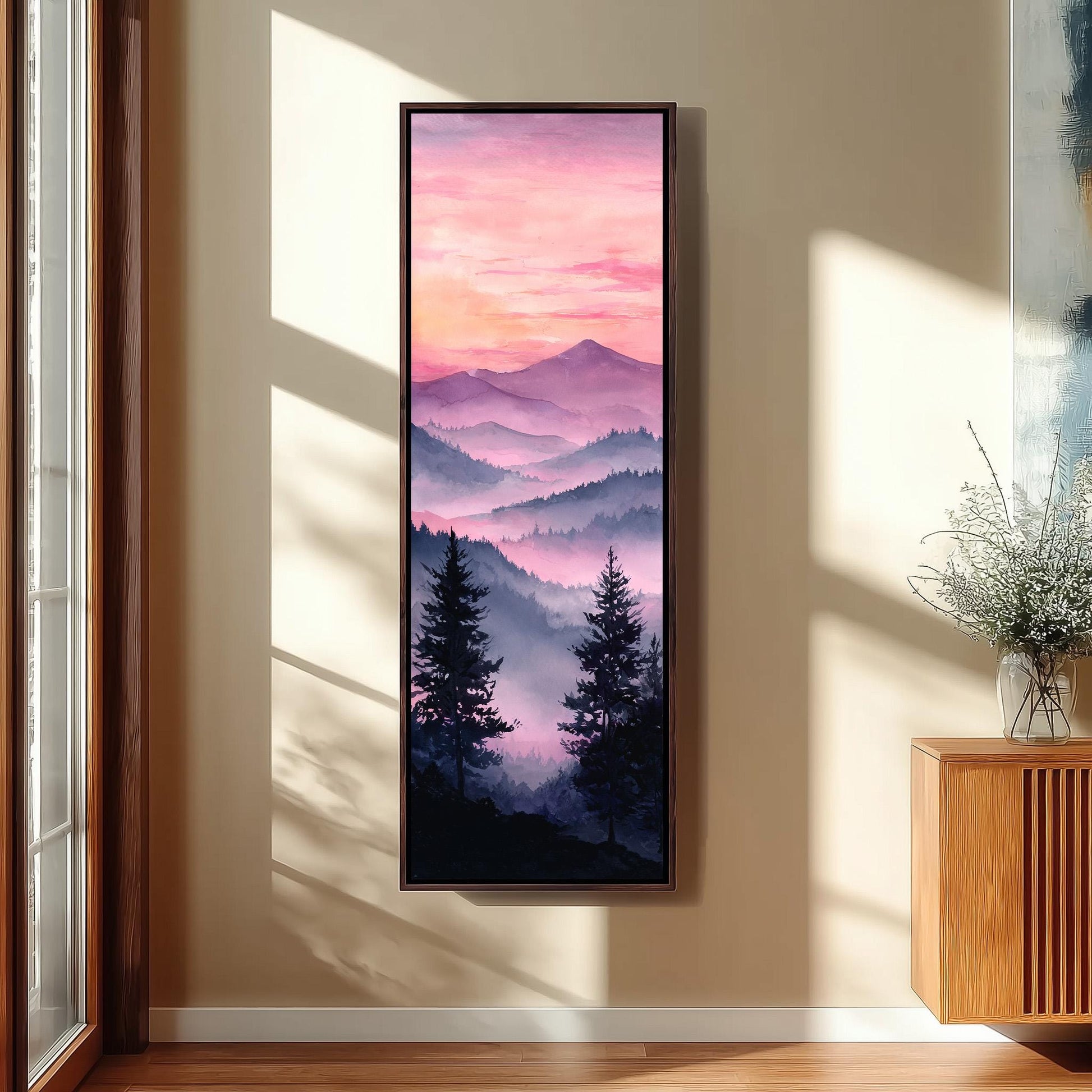 a large framed painting hanging on a wall, depicting a serene mountain landscape with silhouetted trees and a vibrant sunset sky.