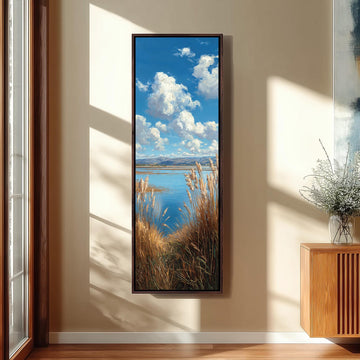 a large framed painting hanging on a wall, depicting a serene landscape with a body of water, mountains, and a sky filled with clouds.