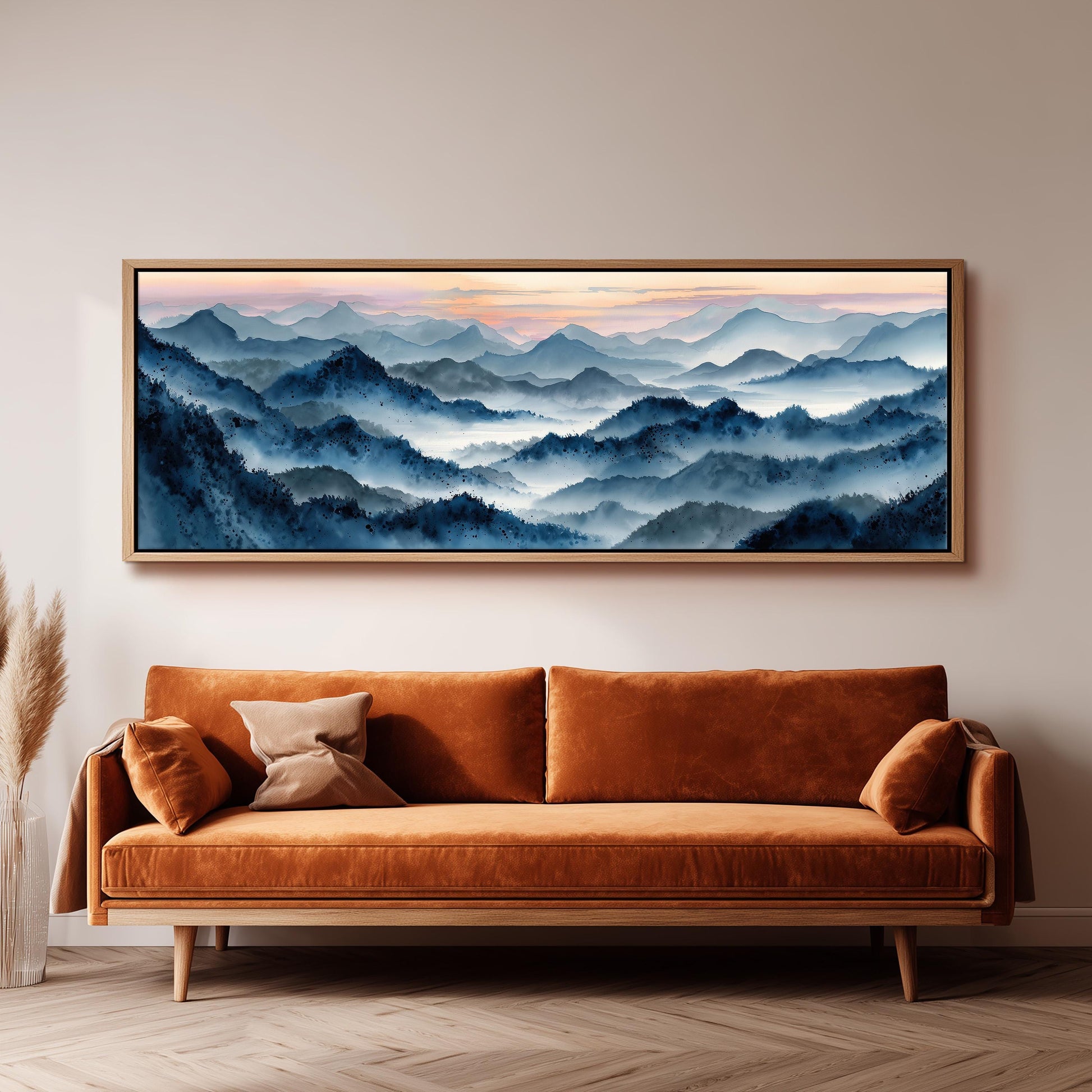 a large, framed painting of a mountainous landscape with a hazy, blue-toned sky above. The painting is hung on a wall above a brown sofa with orange cushions.